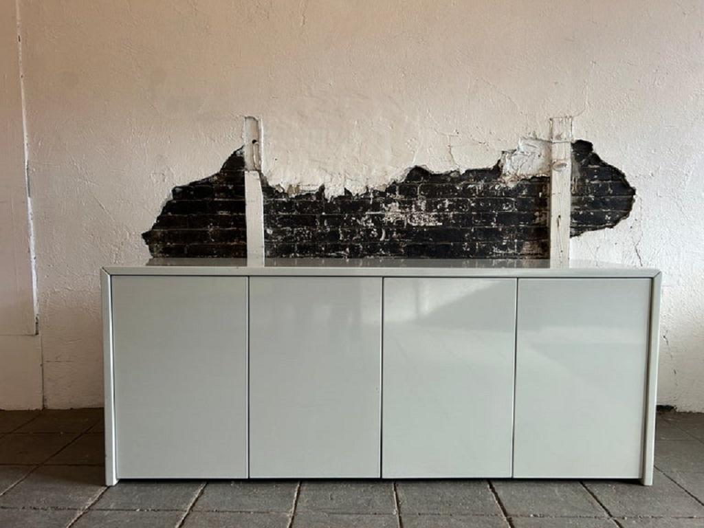 Post modern light grayish/blue Lacquered 4 Door Credenza Cabinet. This 73” wide credenza has storage inside behind 4 door panels with 6 adjustable shelves with all pins inside, has minimalist design for an office, home or studio. Sits on 4