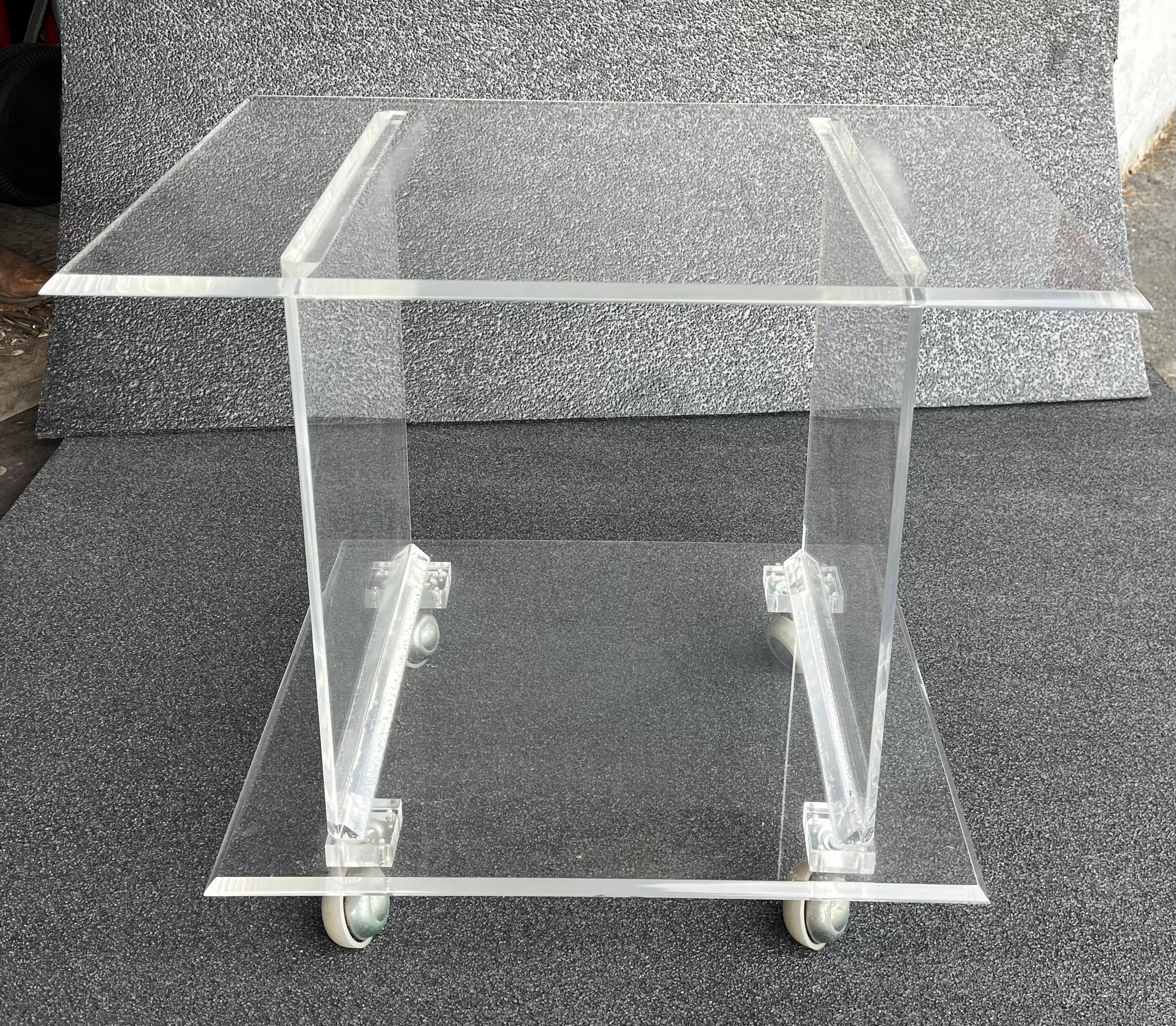 Two tier rolling bar serving cart in thick lucite. This well crafted cart features an overhanging top shelf, with cut beveled edges, over a smaller shelf.
 This example is in very fine, original, clean and ready to use condition. Reminiscent of