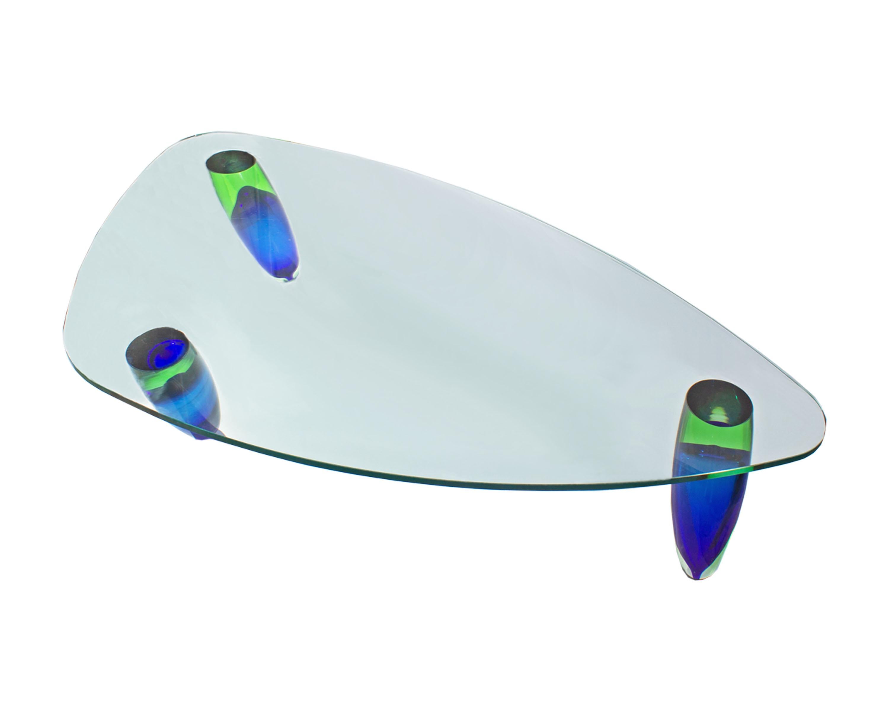 A Postmodern Murano glass coffee table designed by Italian designer Maurice Barilone (born 1947) for Roche Bobois. Three bullet-shaped green and blue legs support a clear triangular-shaped table top with rounded corners. Each Sommerso leg glass