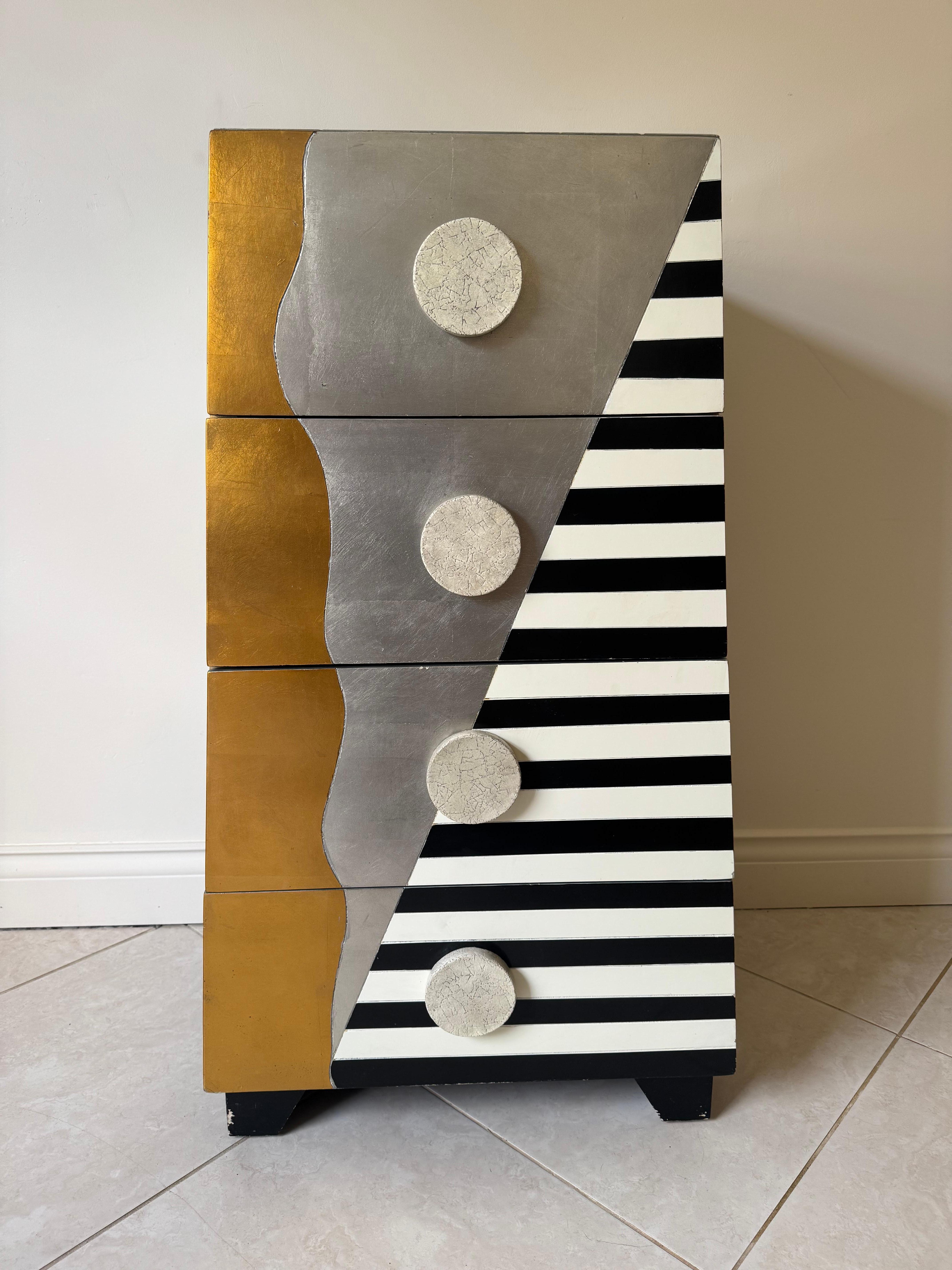 Magnifique commode post-moderne de style Memphis. Fabriquée à la main en Italie, cette pièce remarquable est ornée de feuilles d'argent et d'or.  avec des rayures et des formes qui lui confèrent le motif populaire de Memphis. Les 4 tiroirs disposent