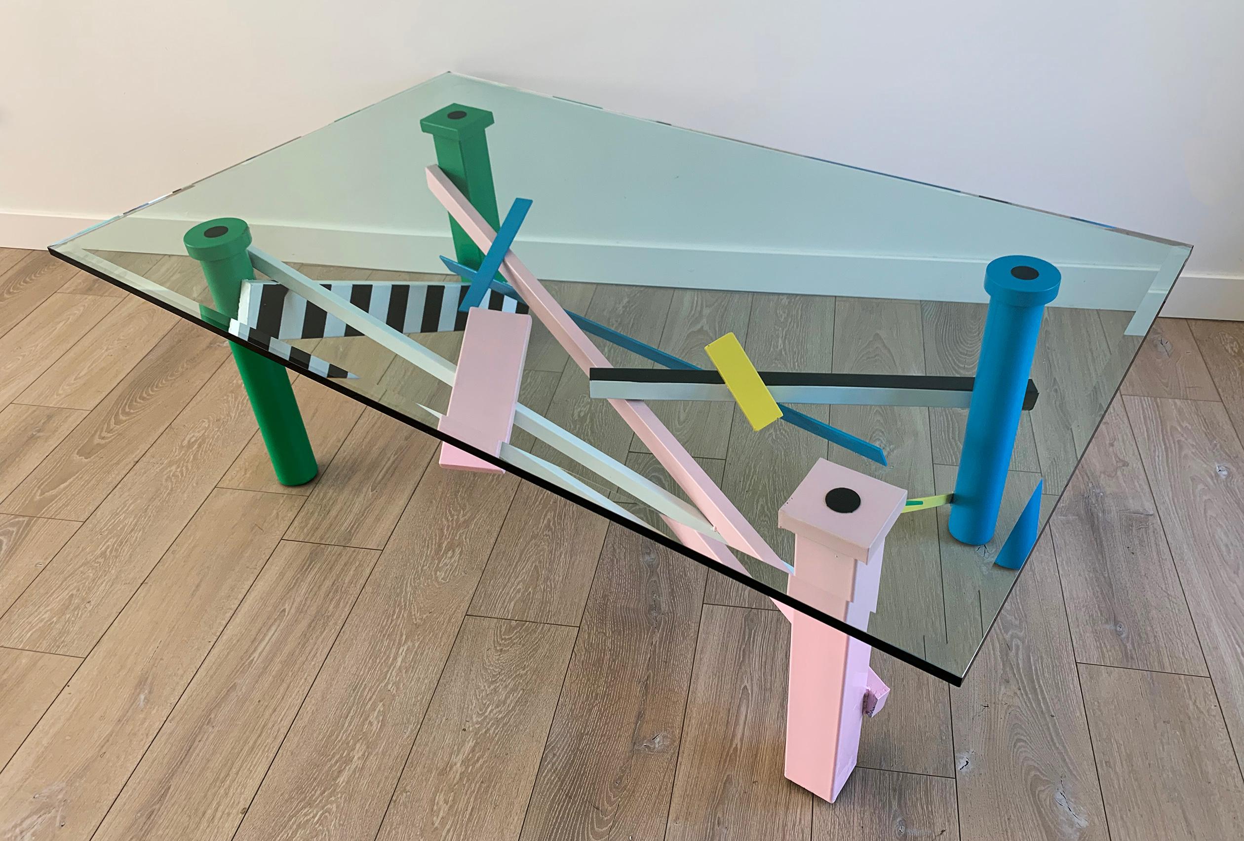 This Postmodern coffee table is a definite conversation piece. The base is constructed of metal that has been welded together into an intricate Postmodern design and lacquered with the same pops of color that helped define the 1990s post modernism