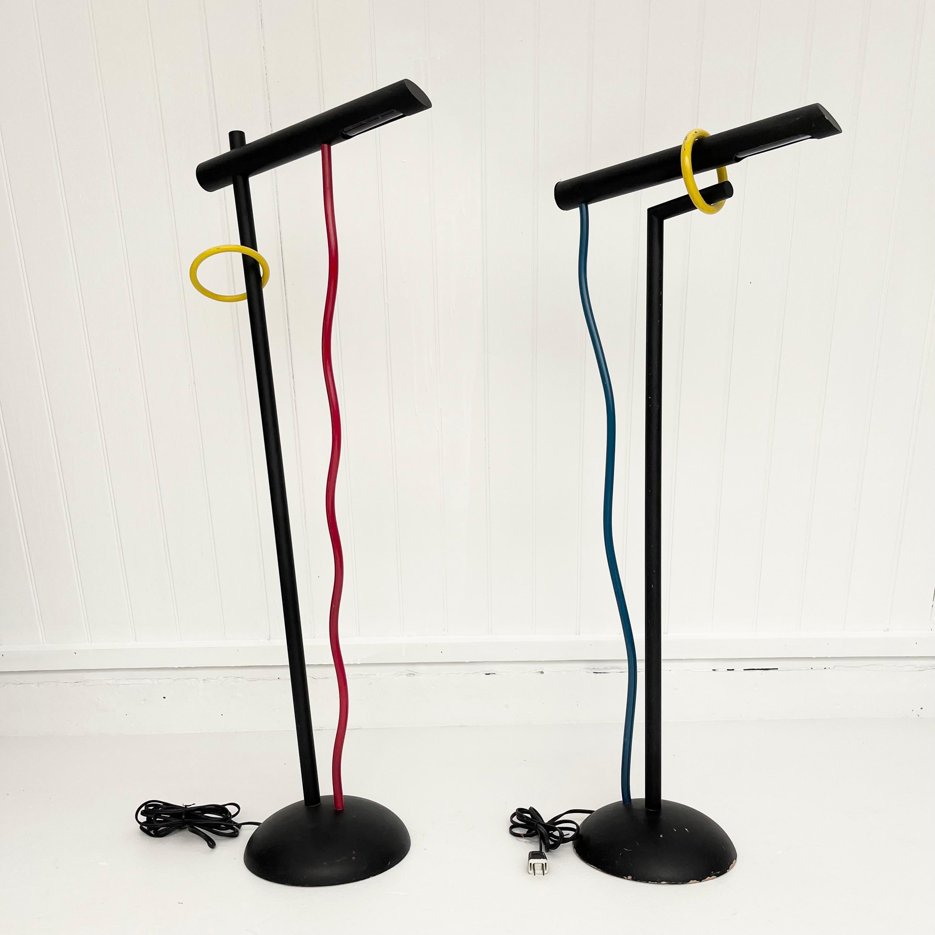 Dynamic pair of 1980s sculptural Memphis-style floor lamps. Both with a black enameled L-shaped body with a wooden base. Each lamp has its own unique abstract linear elements that attach from the lamps' base to the head, both in different colors of
