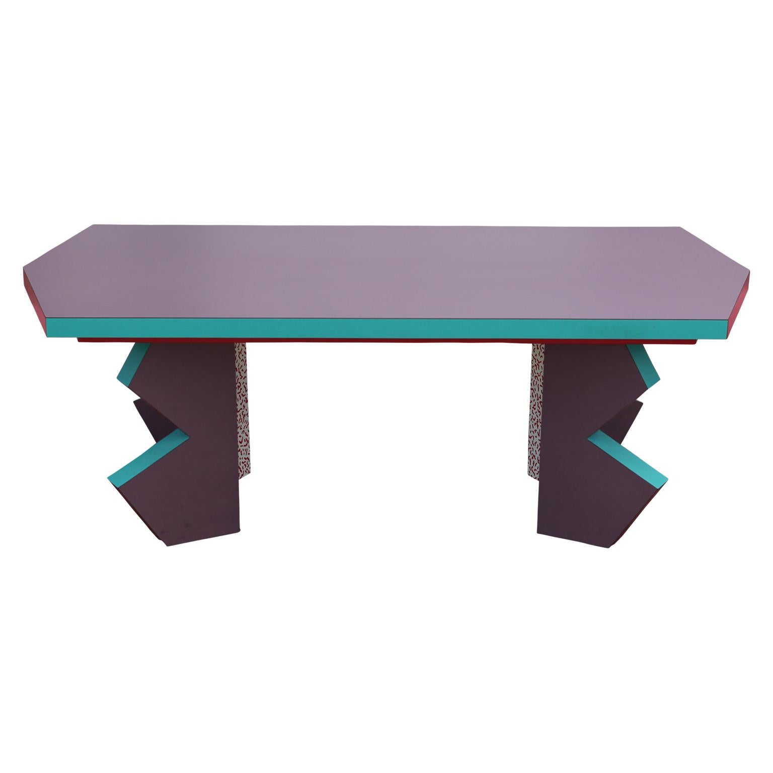 Memphis style pink, teal and purple coffee table with a red and white decorative pattern on the inside of the legs.