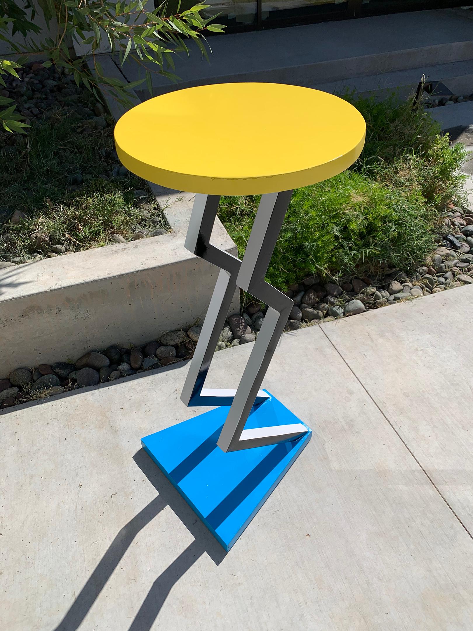 This table is absolutely stunning! A true conversation piece, this 1990s table is in the style of Memphis Milano and features bright pops of yellow and blue with black and white zig-zag legs.

A fantastic table or pedestal accent piece for any