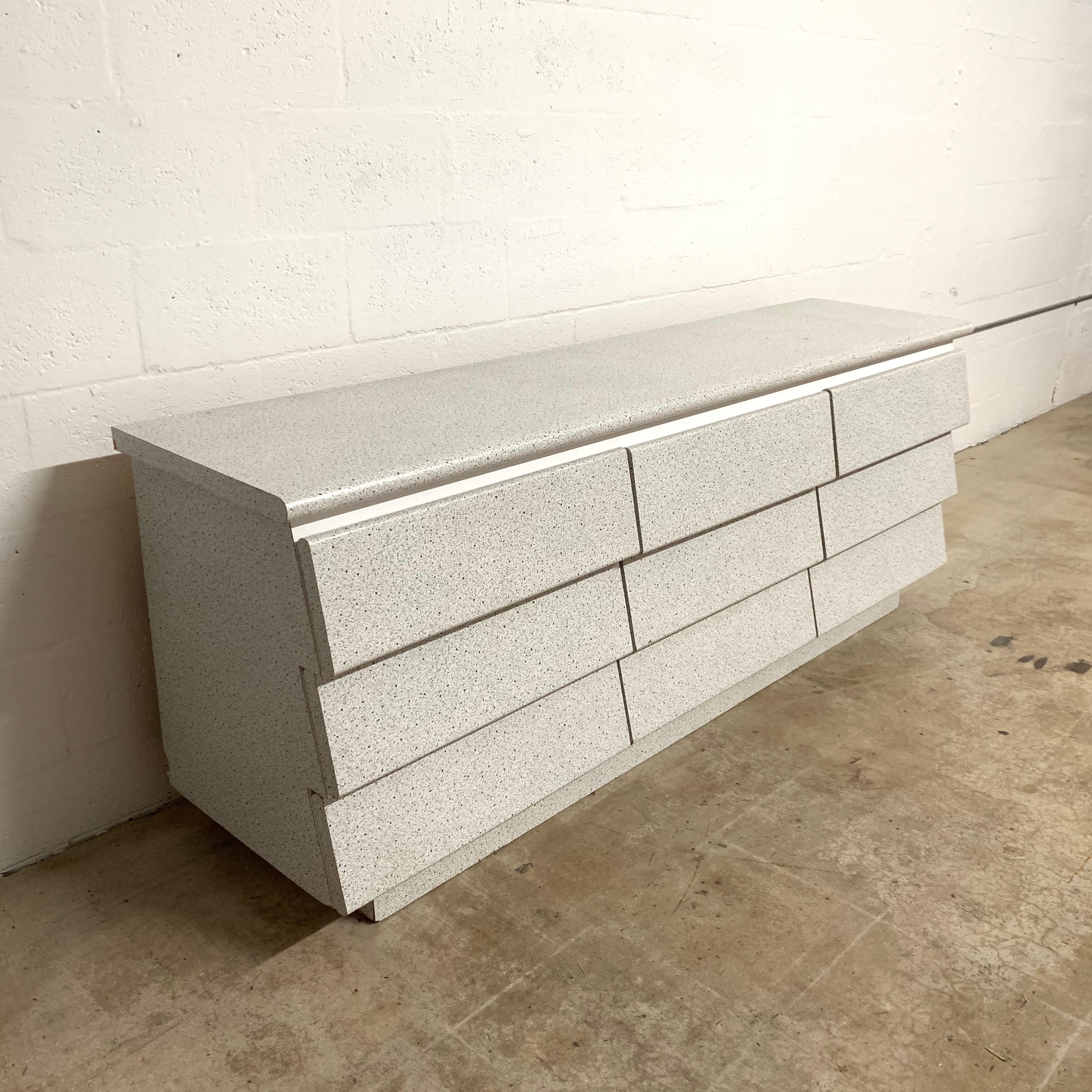 Postmodern dresser or chest of drawers rendered in textured granite and white Formica, with slanted front drawers all on tracks.