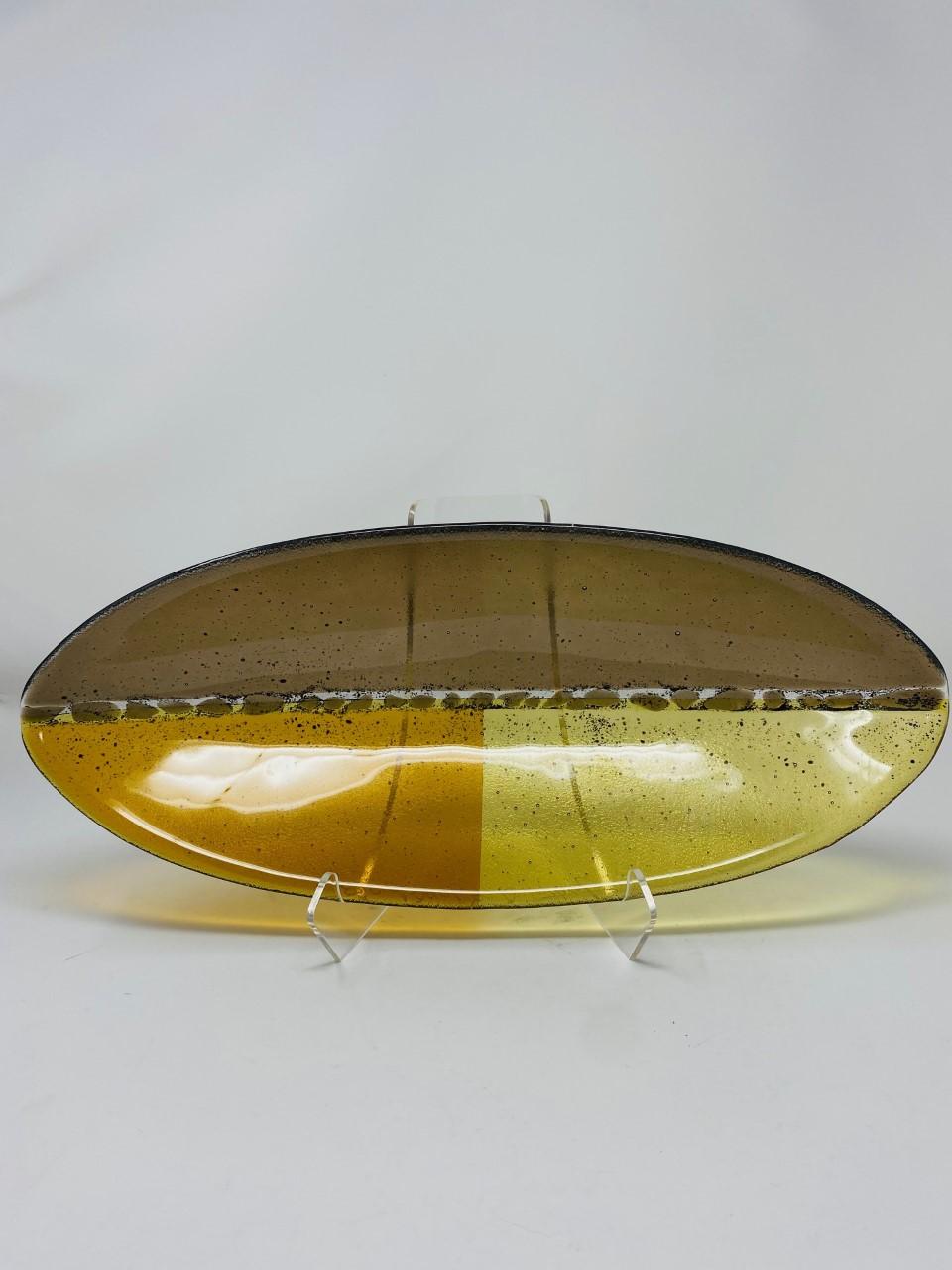 Beautiful and graphic oval glass art bowl by Rosenthal. This beautiful piece from the late 90s is graphic and detailed. It shares yellow and amber tones along with a smoke purple tone in a canoe like shape. The piece is eye catching and minimal. A