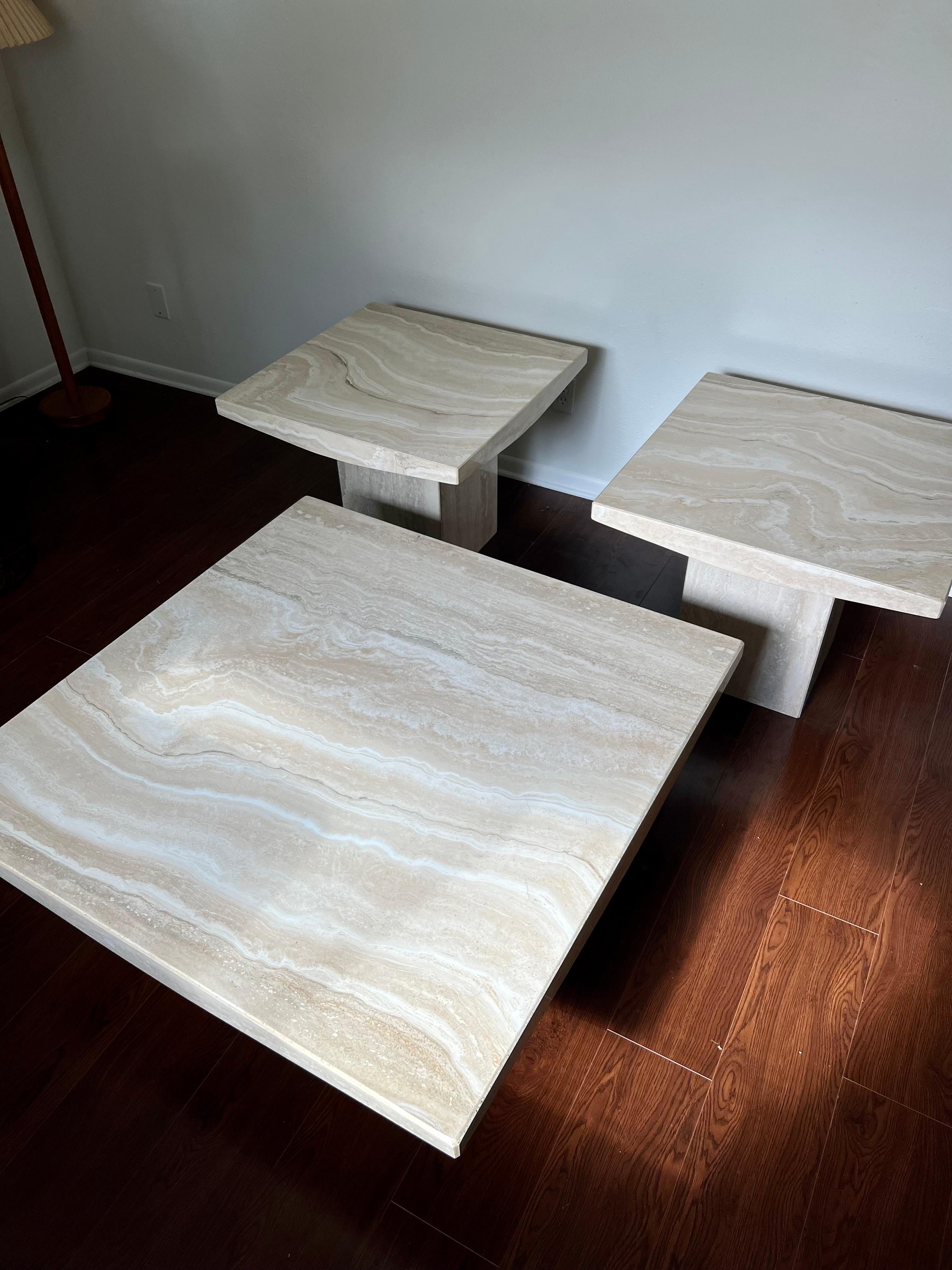 A set of Italian travertine side tables by Stone International. Beautiful side tables in polished travertine sitting on a square base. Has a very nicely shaped top with curvy edges. Overall in very good condition with some very minor chipping on the