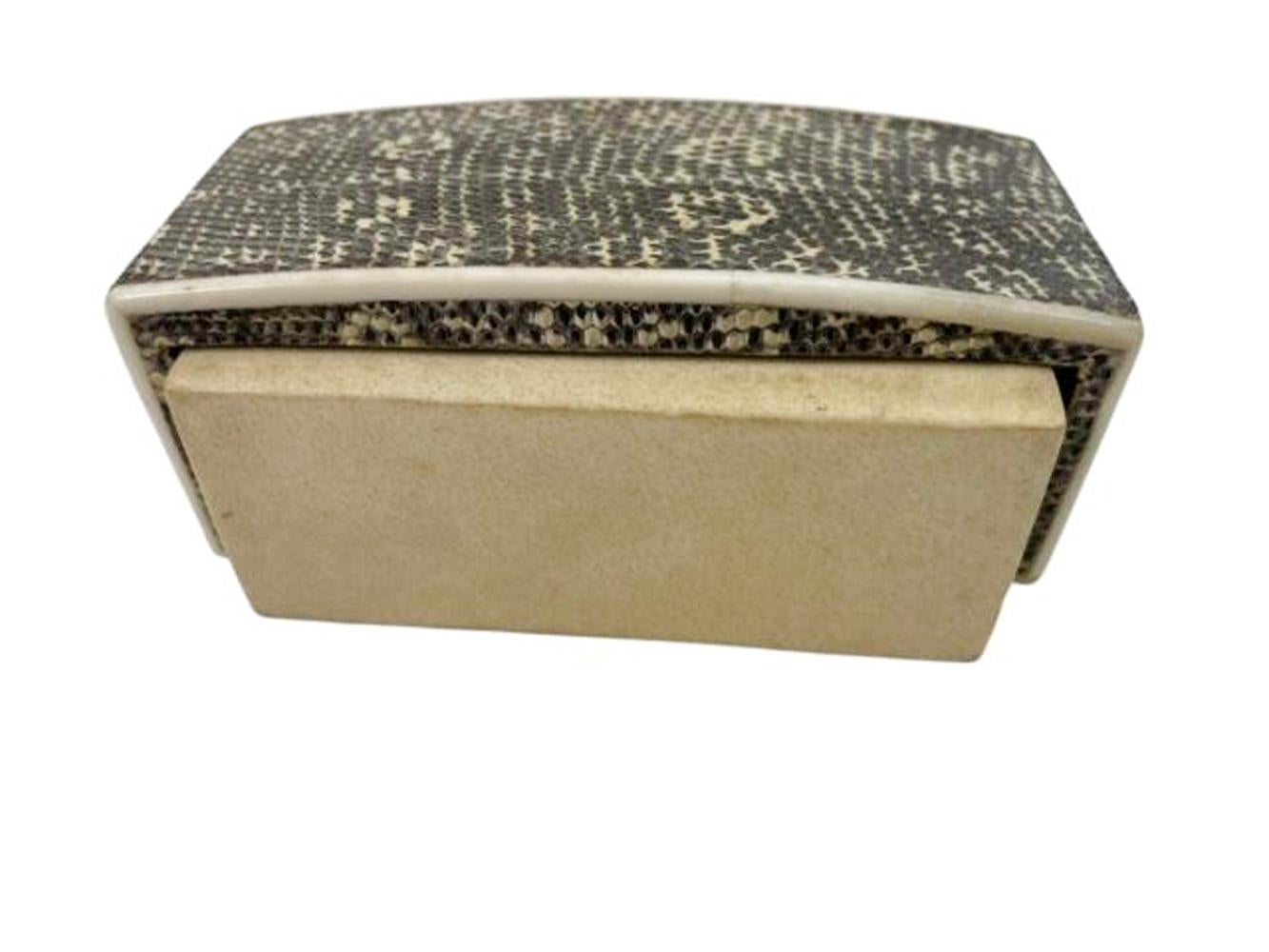 Caja de tapa abierta envuelta en pergamino y con tapa que tiene la parte superior arqueada y continúa por los lados cortos envueltos en piel de serpiente con bordes de hueso conformado. Marcado en la parte inferior R&Y Augousti - París. 