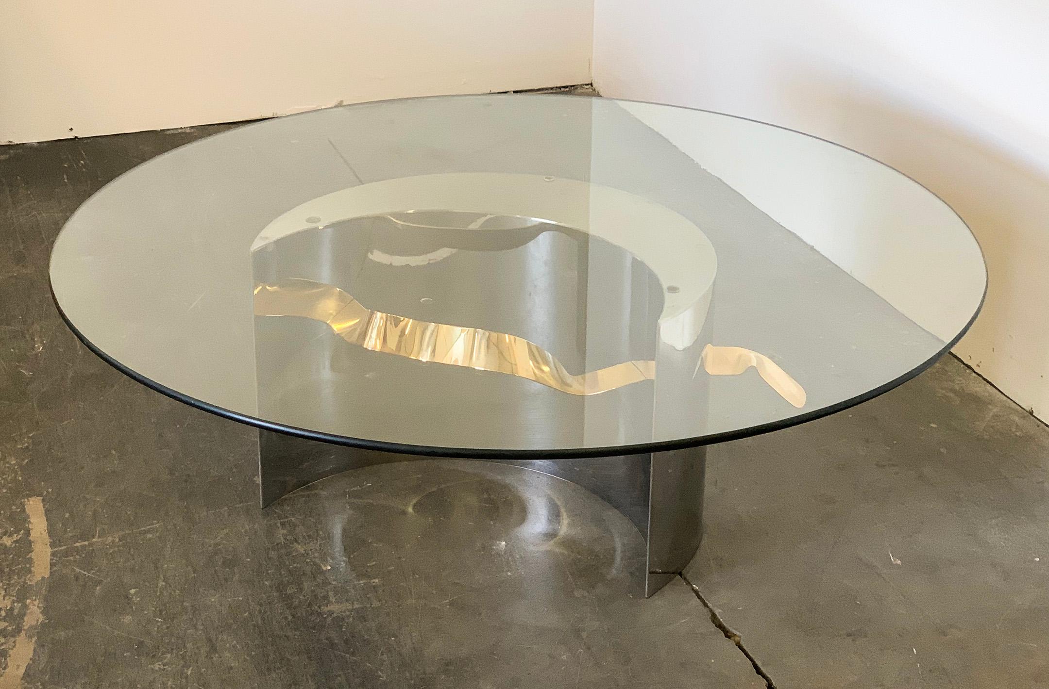 Available right now we have a gorgeous Postmodern dining table that is made of polished stainless and brass. The table features a polished stainless crescent shape, and is set off right with an undulating brass ribbon that goes through the piece.