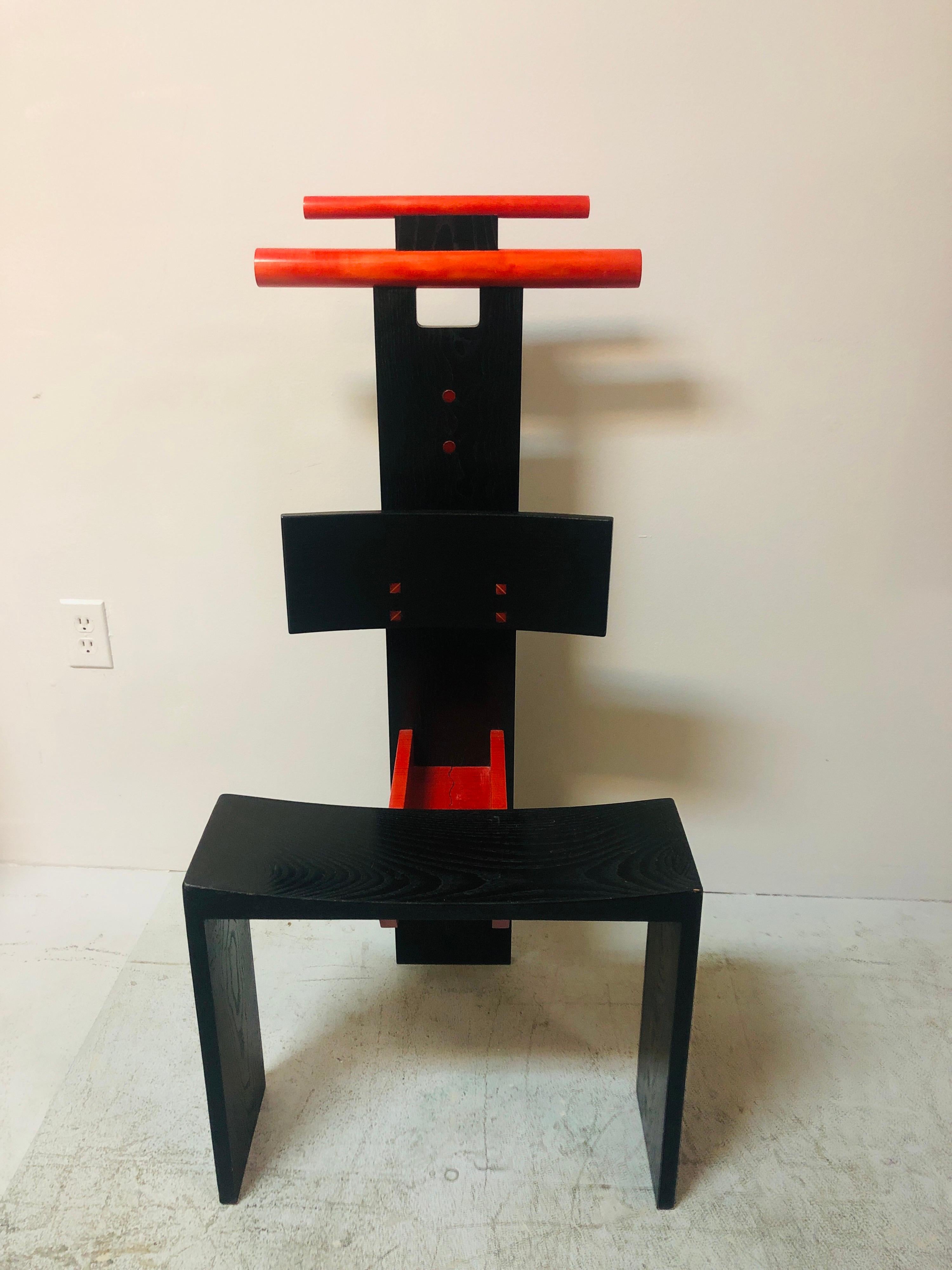 Una sedia post moderna o una valletta. Un design spettacolare che eleva un mobile pratico al regno dell'arte. Accenti colorati che ne accentuano lo scopo, come i 2 scomparti aperti sui piani orizzontali e i 2 tasselli dentellati sul retro.