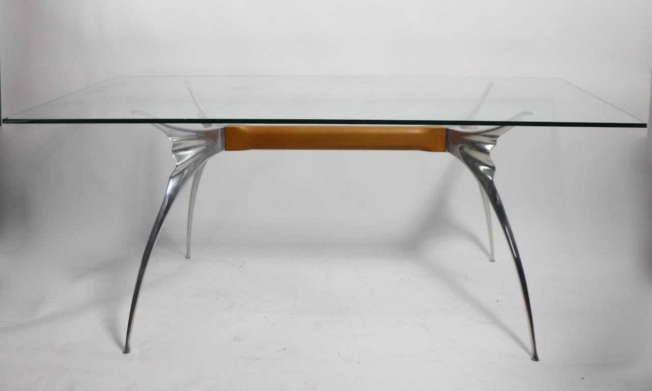 Voguish, chic Postmodern glass top table, desk designed by Bernard Dequet for Protis, made in Paris, France circa 1980s. Stylized aluminum arms connected by beech wood center support, on which rests a rectangular plate glass top ( .5 in. thick ).