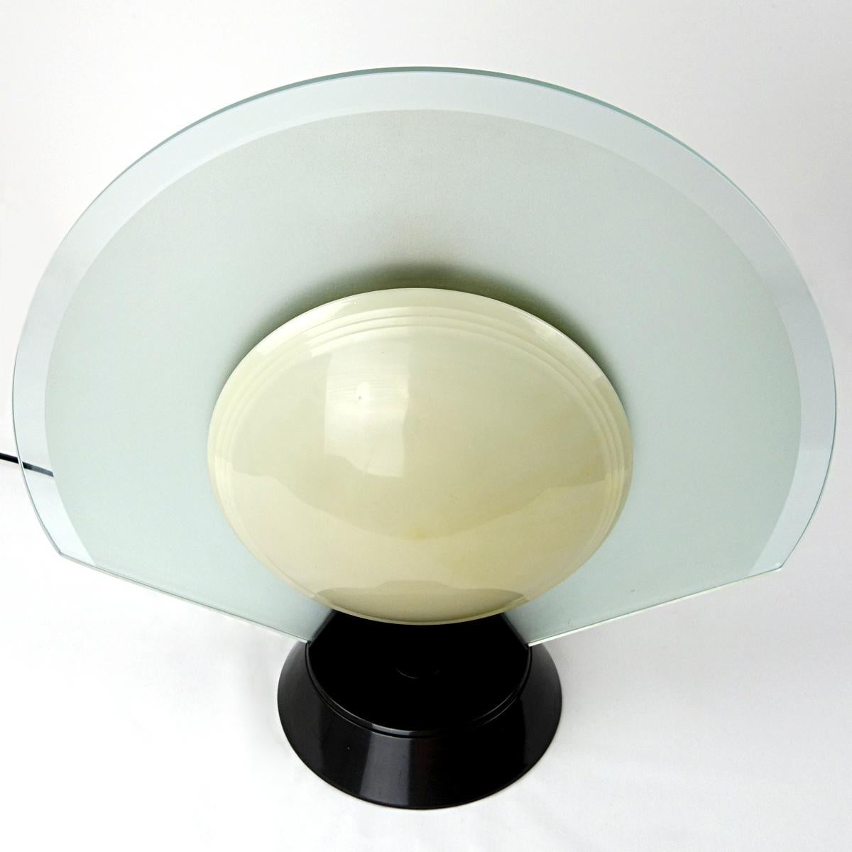 Table lamp Tikkal was designed by Pier Giuseppe Ramella for Arteluce circa 1980.
The fan shaped frosted glass shade may rotate on its base showing either an off-white convex plastic lens on one side or a soft gray lens on the other.