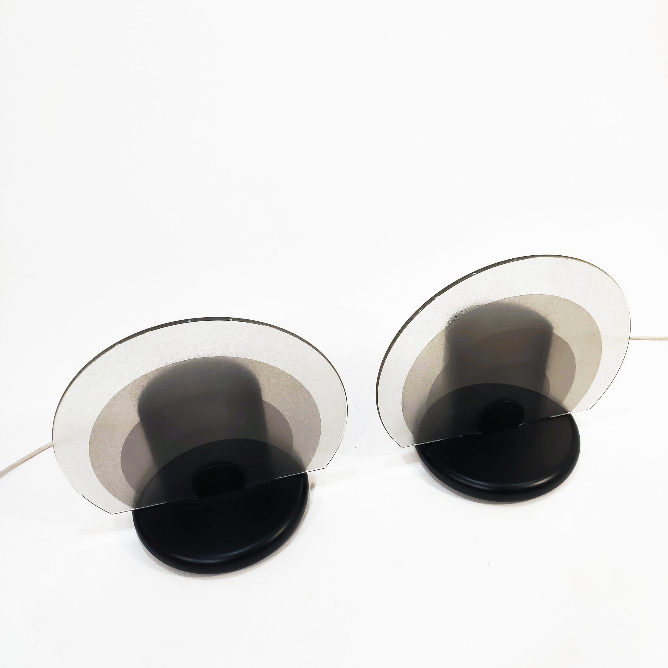 Pair of Italian table lamps attributed to Bruno Gecchelin, 1980s. Made of perforated metal lacquered in black and circular glass diffuser finished in 4 different tones, embodying the modern Italian style of the 80s. 
Very much in the style of other