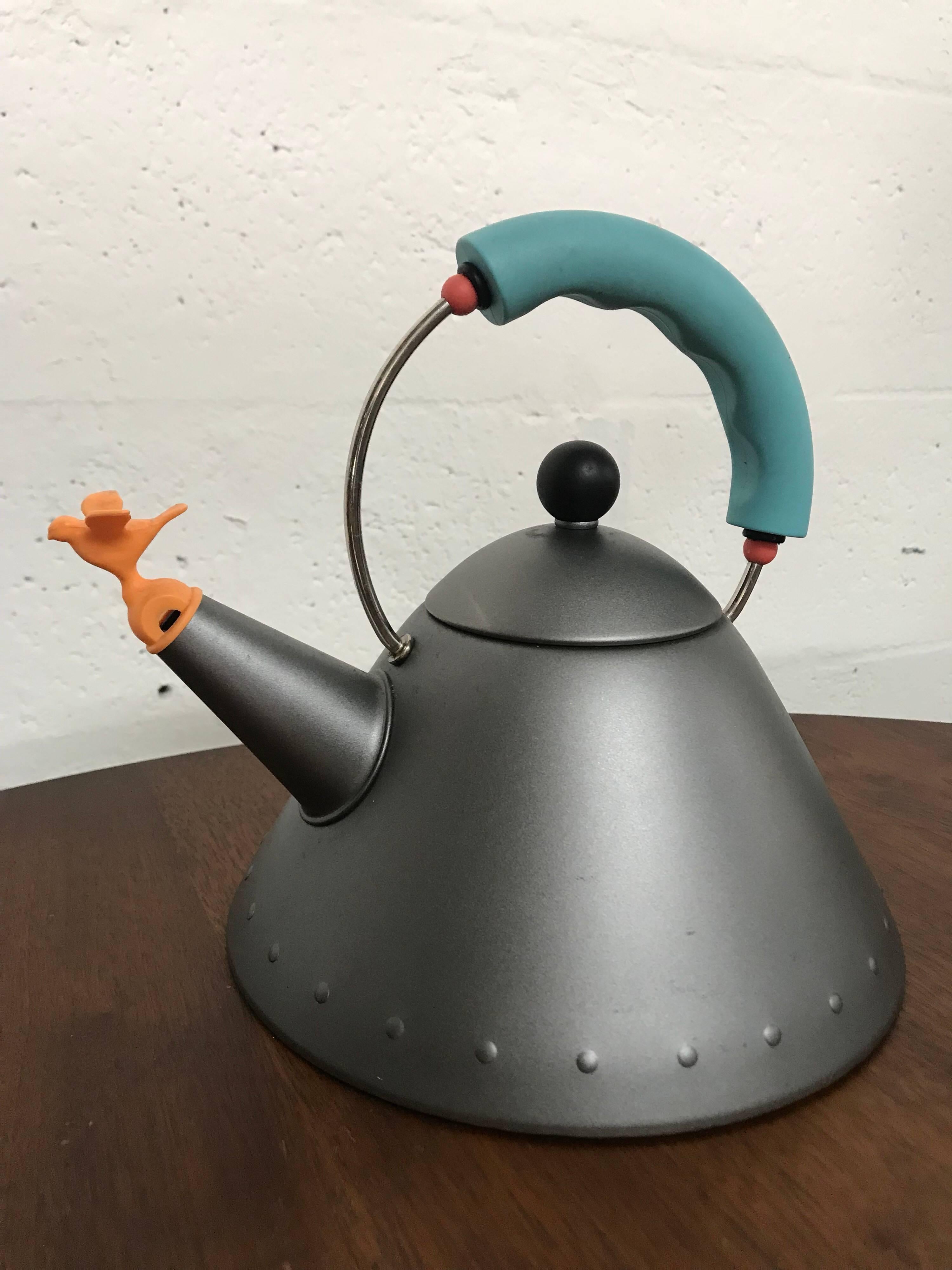 Michael Graves Postmodern tea kettle for Alessi rendered in matte platinum grey enamel body, black knob, orange whistle bird and turquoise handle with red appointments.