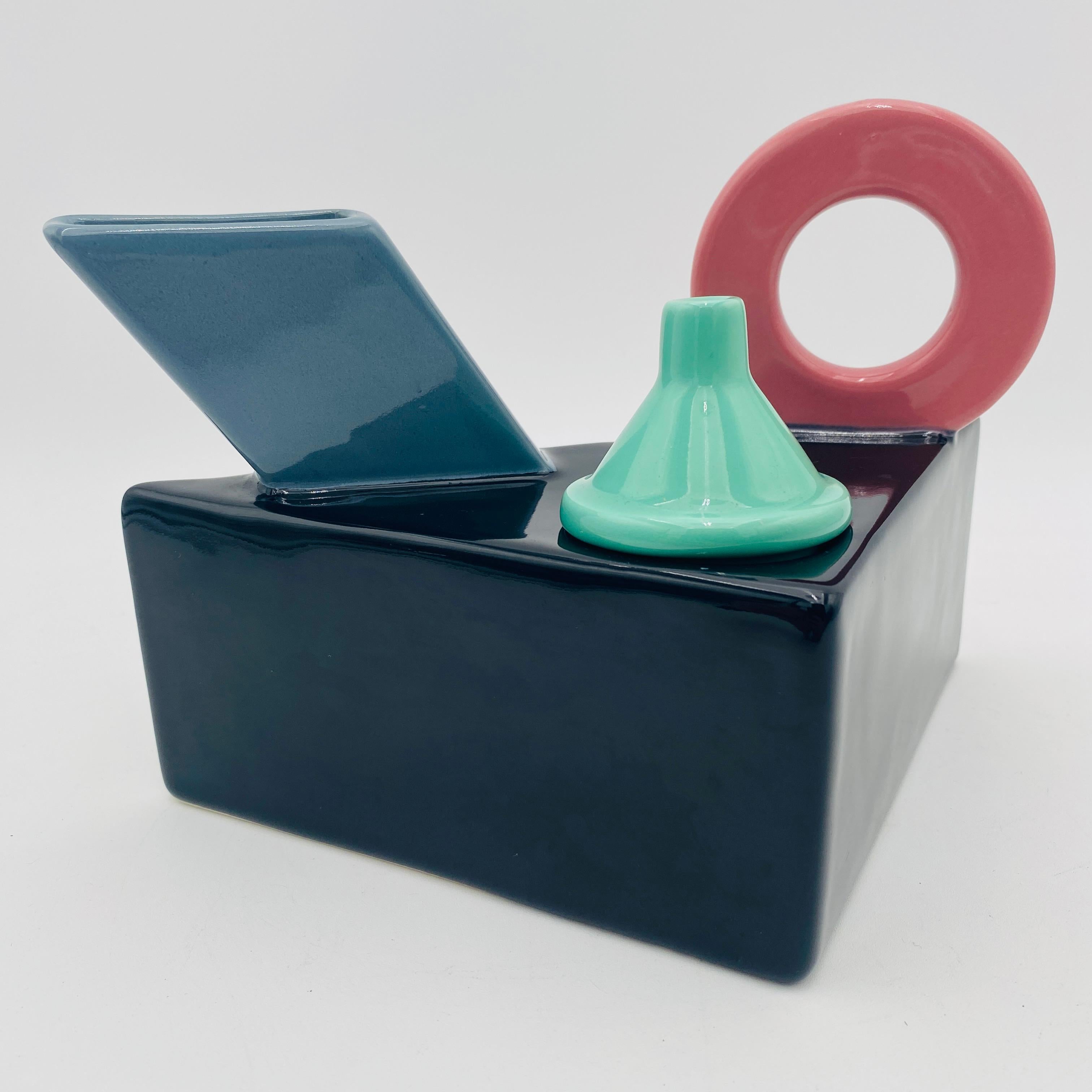 Tetera de porcelana posmoderna diseñada por Peter Langer para Feltman Langer. Es del estilo de Peter Shire y a menudo se le atribuye. La tetera es asimétrica con adornos geométricos en la parte superior. Los colores brillantes del esmalte combinan
