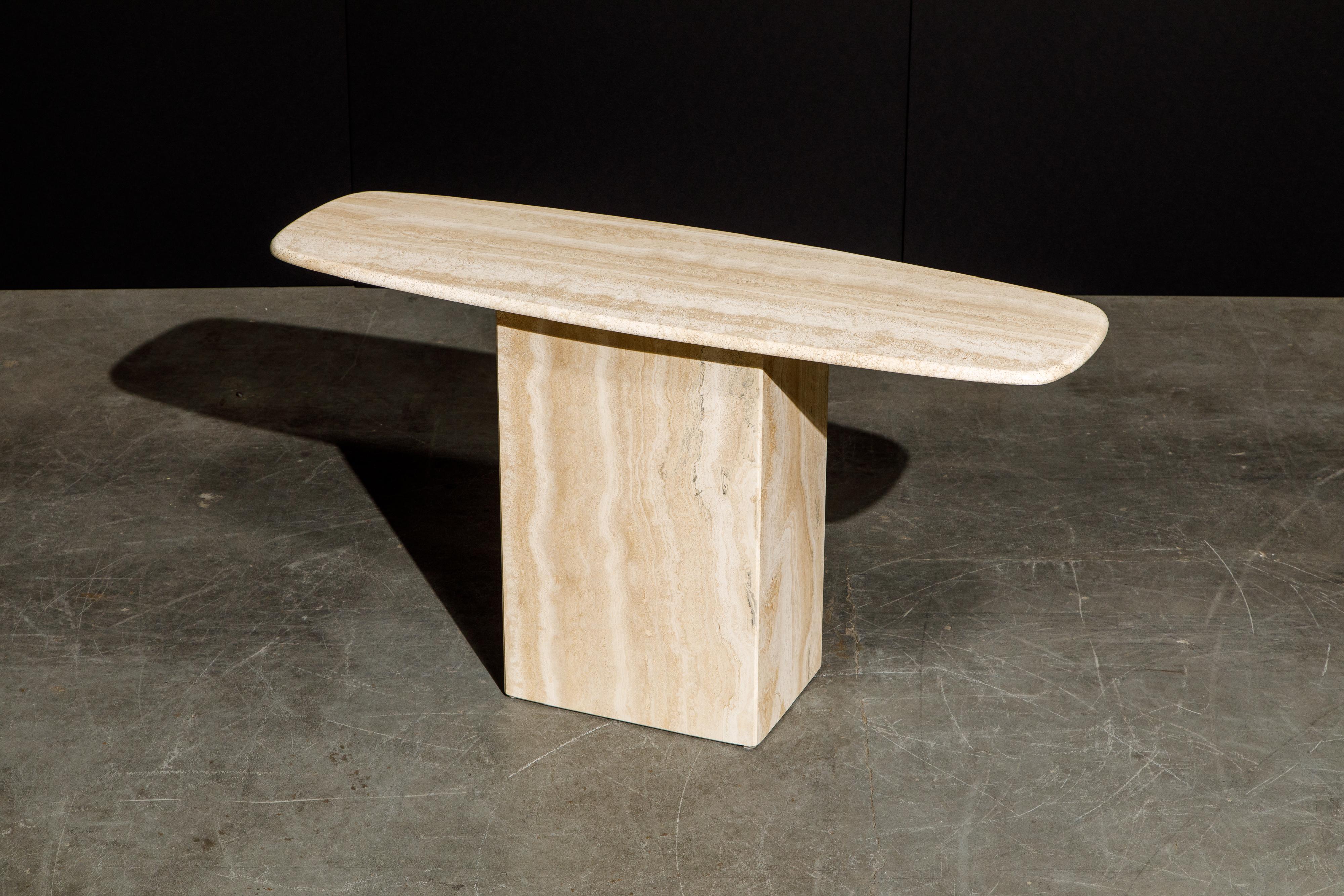 This beautiful Post-Modern Travertine console table, circa 1980s, has beautiful graining and smooth rounded surfboard shaped top. The base has squared edges giving it a contrasting architectural look to the smooth rounded top. 

This sculptural