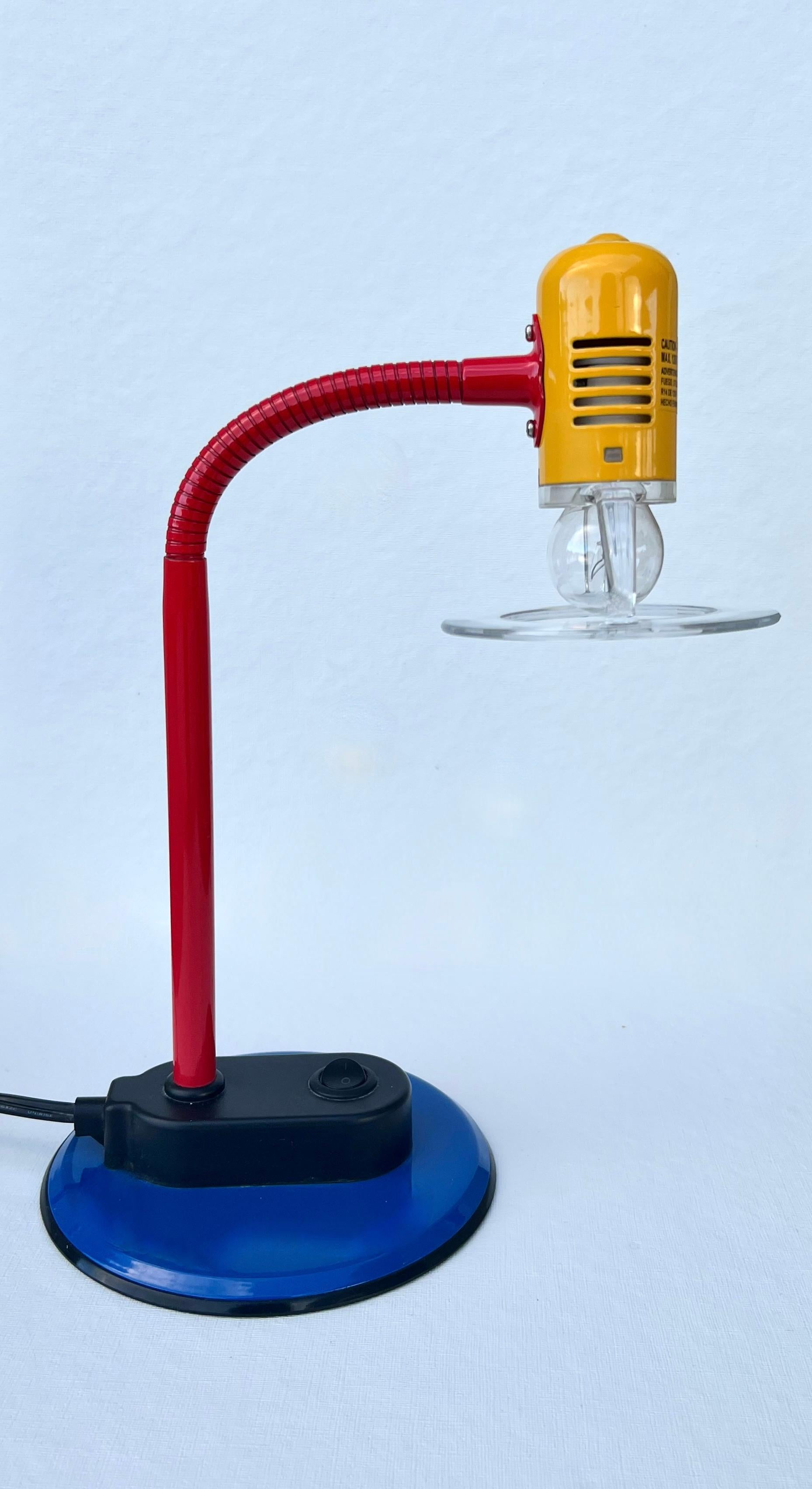 This is a rare, post-modern, 1980s Memphis-style gooseneck table lamp with a bright red, blue, and yellow lacquered metal frame and a plastic clear halo shade. It has a fully adjustable gooseneck that can be positioned according to your preference.