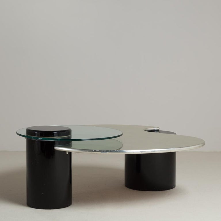 A post modern coffee table with jet black lacquered drum bases with a silver leafed biomorphic table top cut into the side and supported, complete with a rotating circular glass tier top, 1980s

Lacquering carried out in UK workshops while the
