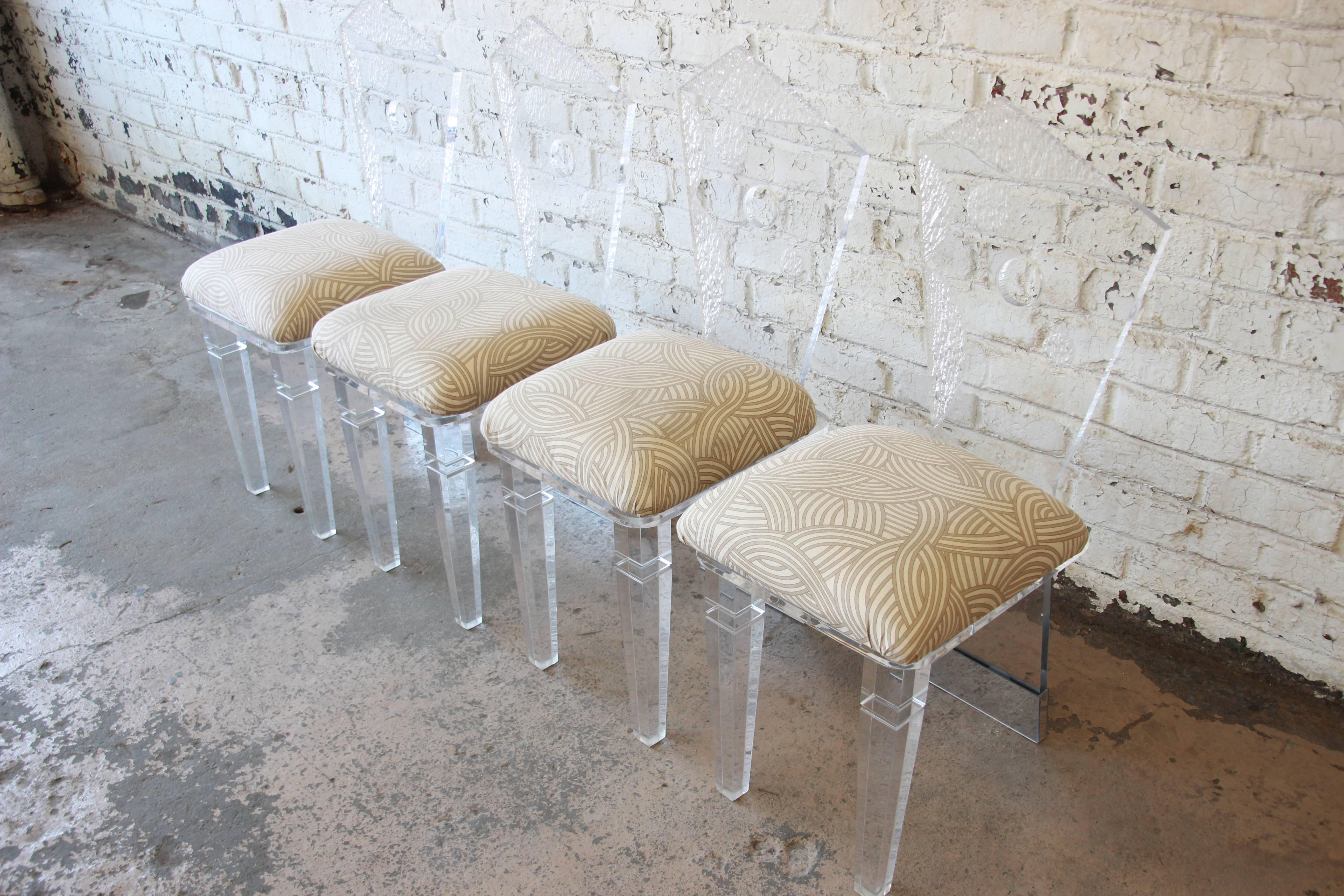 A very unique set of four Postmodern Lucite dining chairs. The chairs feature a unique abstract geometric design. The base at the back is mirrored. They chairs have been reupholstered in tan and cream upholstery. They are solid, sturdy, and in good