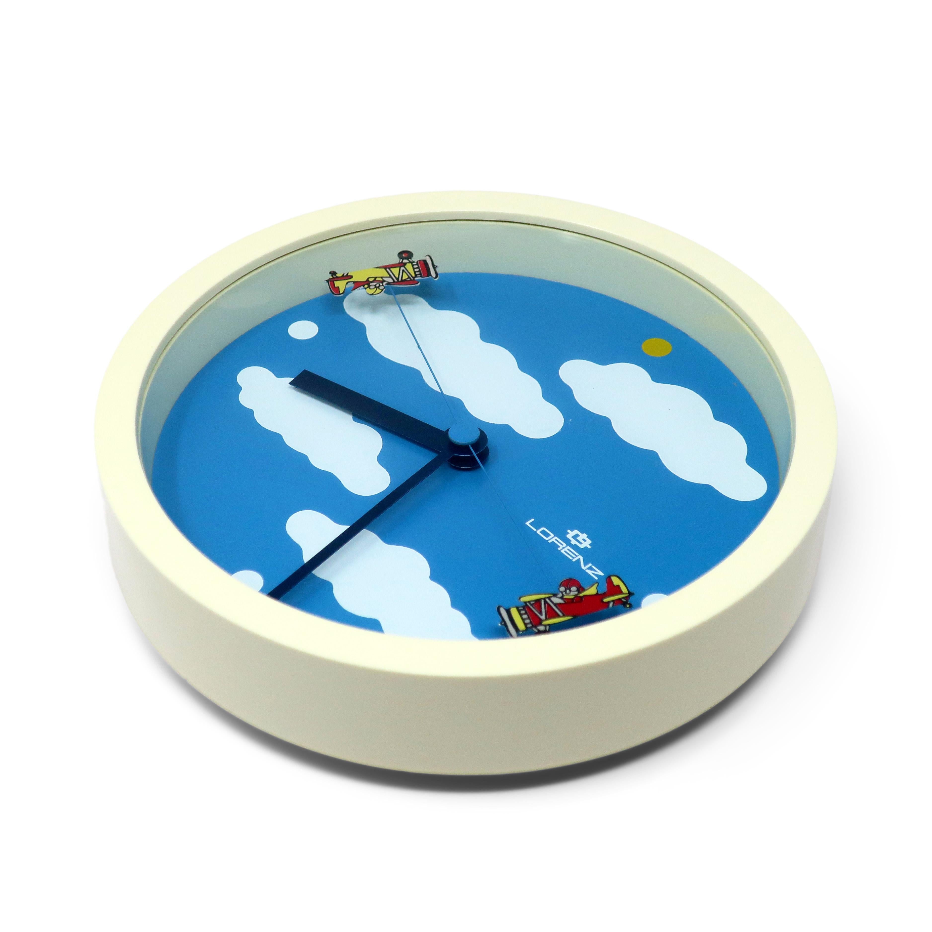 A round 1980s wall clock by Lorenz with white case, blue face with white clouds, black hour and minute hands, and second hand with two bi-planes on either end of the hand.  The clock has white dots for the 3, 6, and 9, as well as a yellow dot at 12,