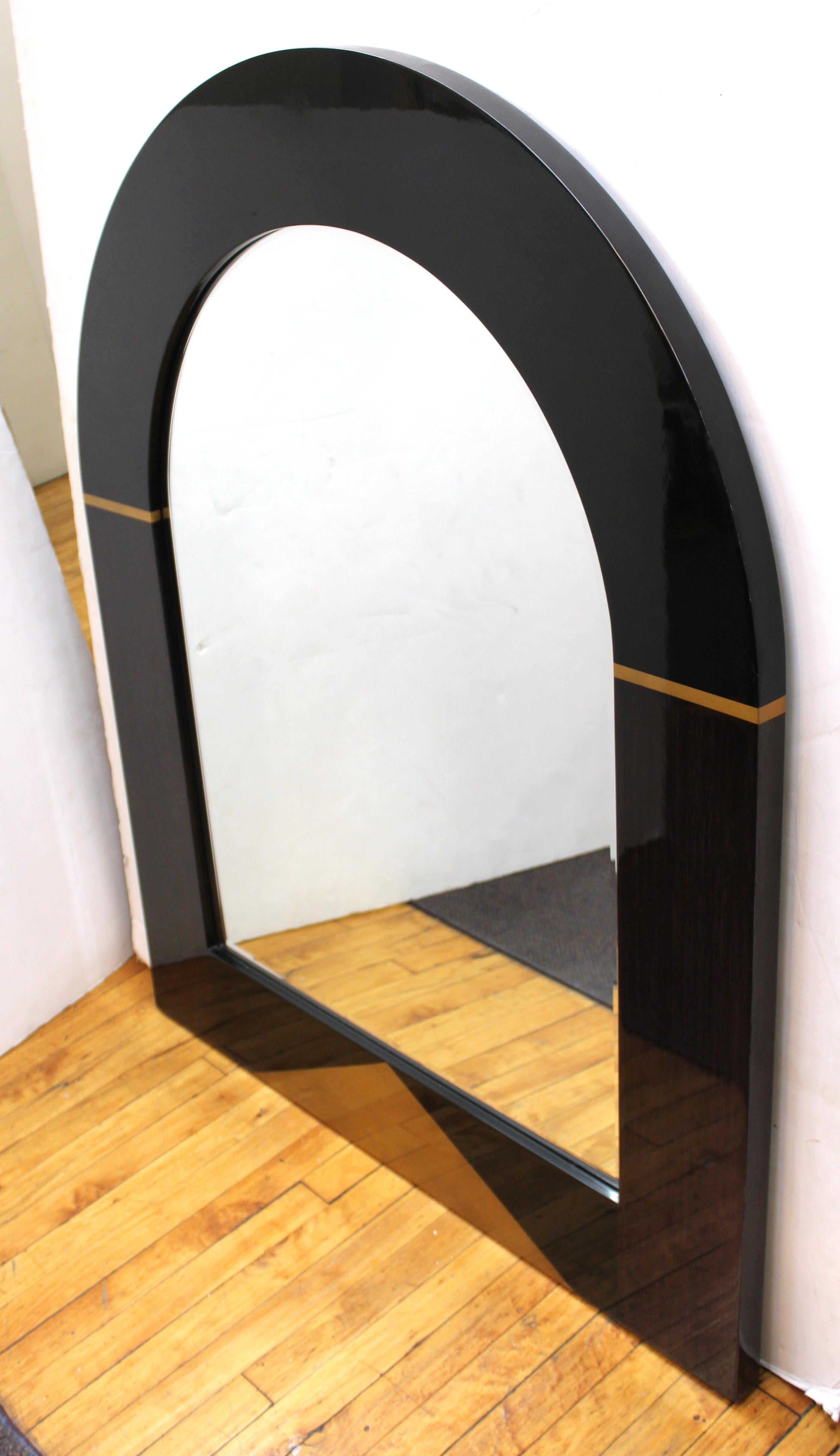 Postmodern mirror with arched top, dark wooden veneer with decorative gilt geometric accents and a lacquered finish. The piece was made in the United States during the late 20th century and is in good vintage condition.