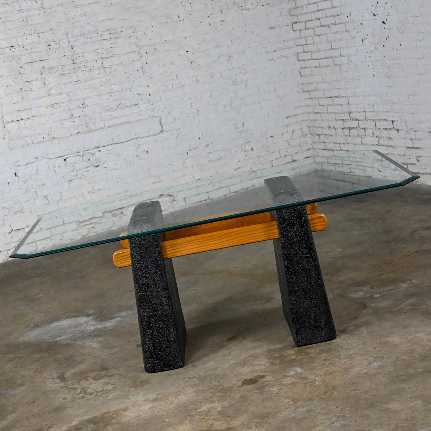 Handsome vintage Postmodern Architectural dining table comprised of a molded plaster double pedestal base with a black stucco textured finish, solid oak cross bars, and a rectangular 1 ¼” beveled 3/8” thick glass top with angled corners. Beautiful