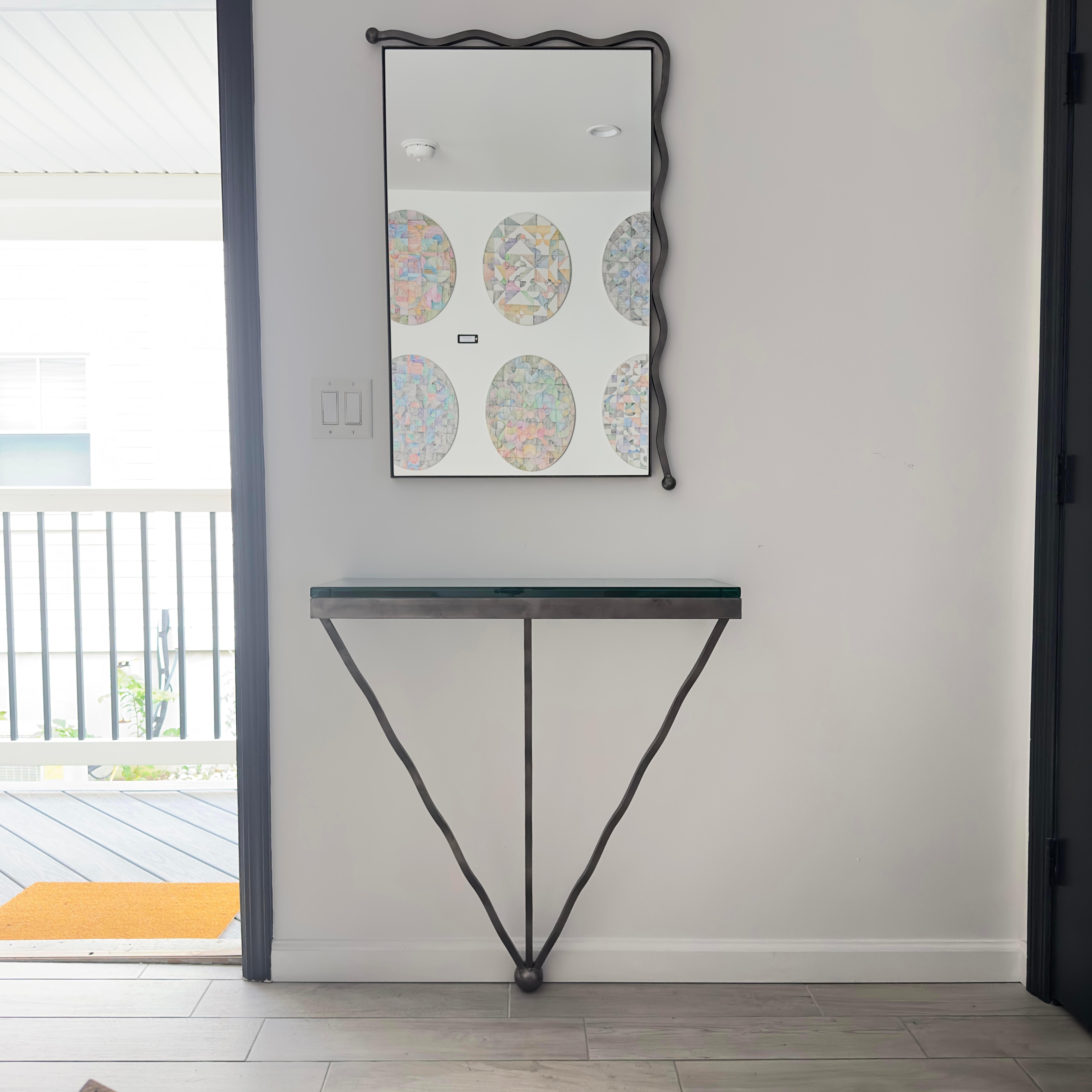 Artist Studio (Gerbone Studios) marked wall-mounted iron postmodern table with glass top and matching mirror. The table mounts to the wall at the top and the bottom sphere rests as a foot on the floor. The glass top is thick and heavy and sits on