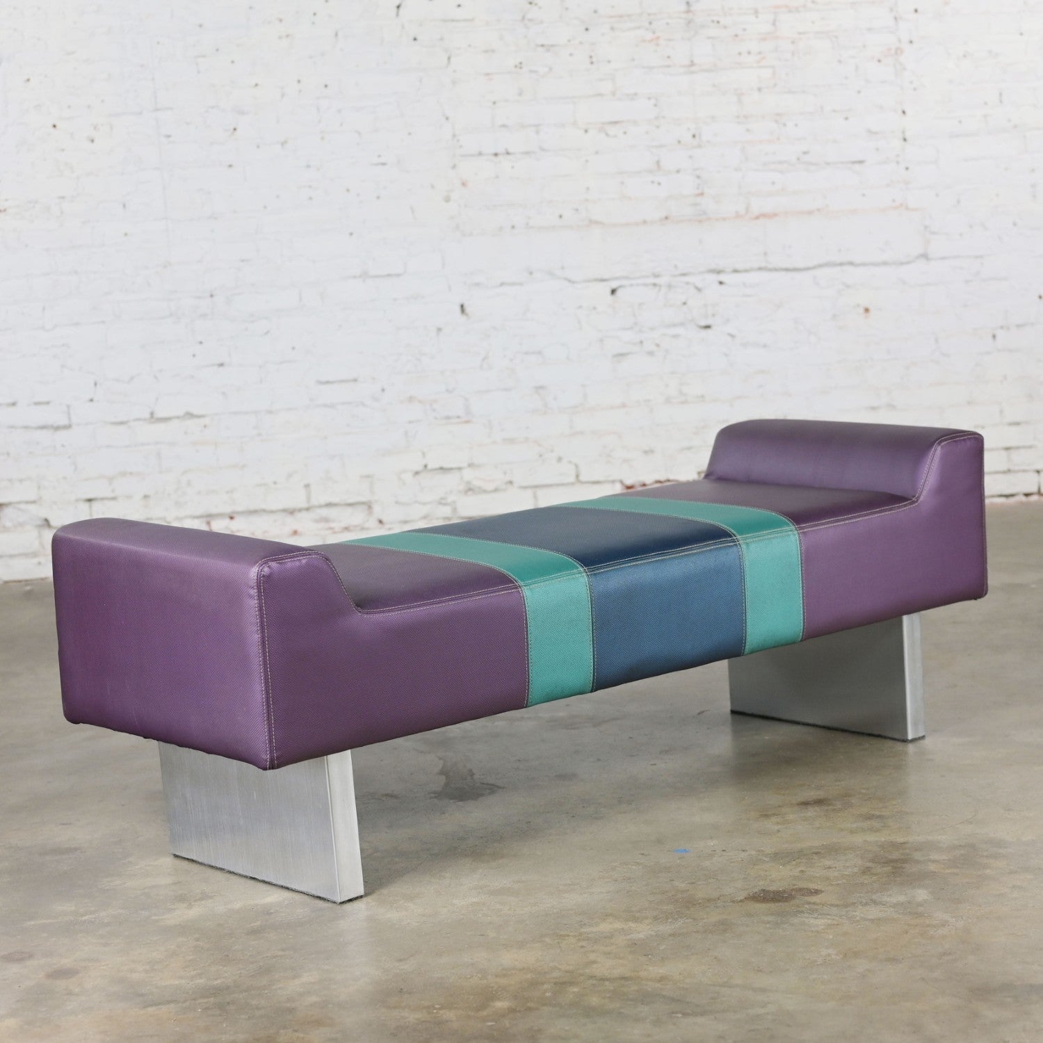 Awesome vintage postmodern bench or settee reminiscent of The Memphis Group. Comprised of a purple vinyl upholstered foam cushion with turquoise with a blue center stripe and extruded brushed aluminum base. Beautiful condition, keeping in mind that
