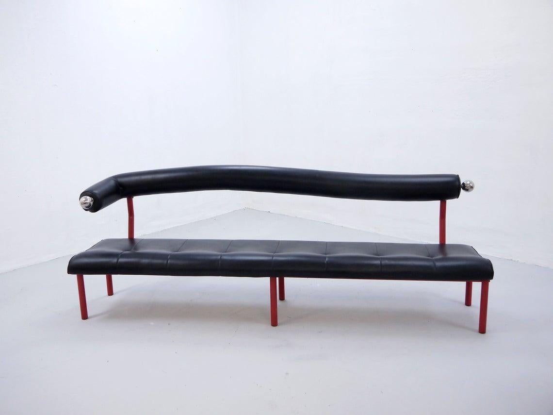 Large vintage sofa bench with black faux leather (vinyl) seating, curved backrest, red-lacquered metal frame and chrome decorations

Unknown origin

Beautiful Postmodern 1980s design

The bench is in very good original condition, with few