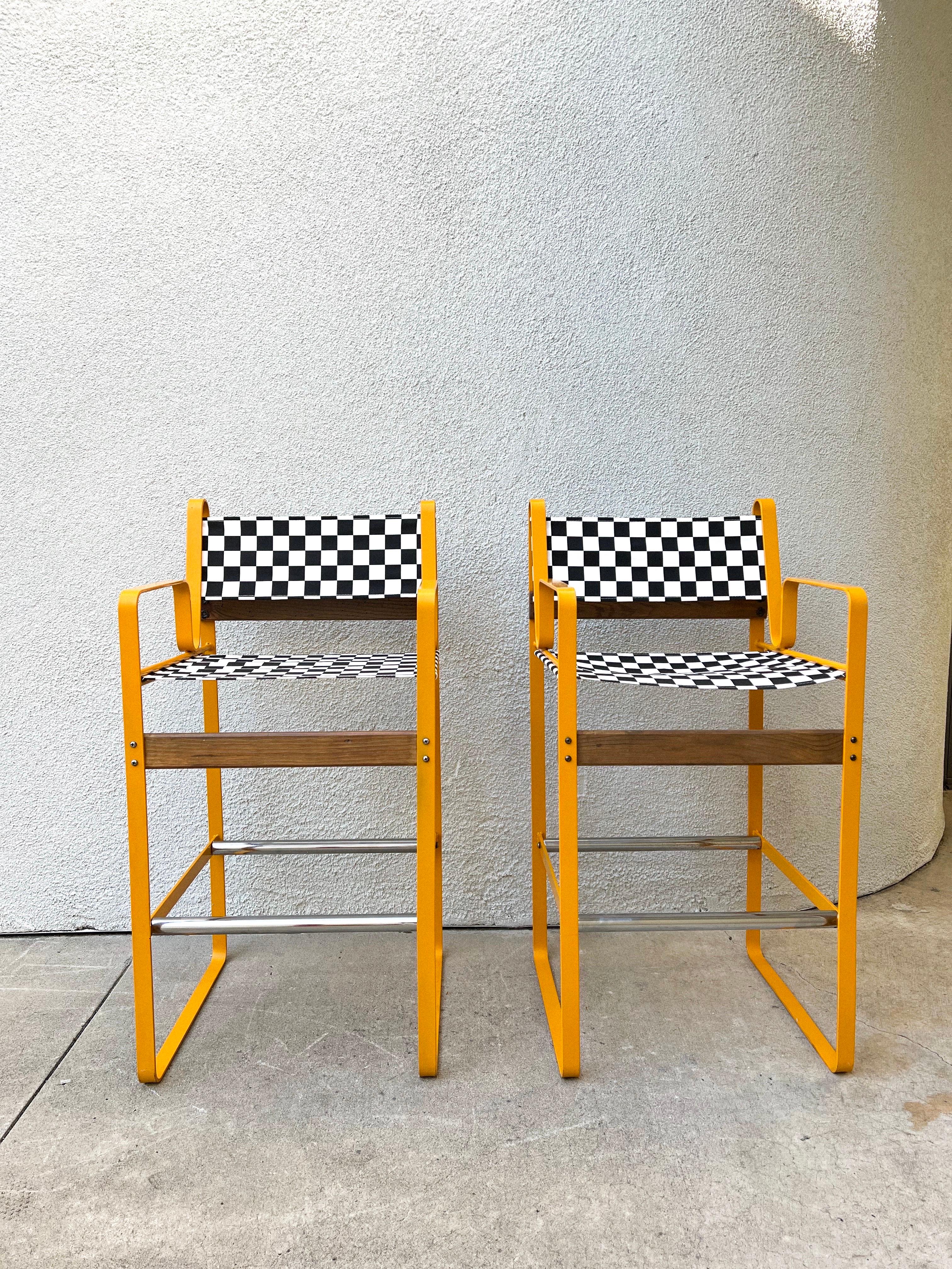 A pair of postmodern barstools in the manner of Bruno Pollak. These stools feature a very sturdy metal frame coated in orange, chrome footrests and wooden support bars. Seats and backs are brand new cotton canvas in a black and white checkered