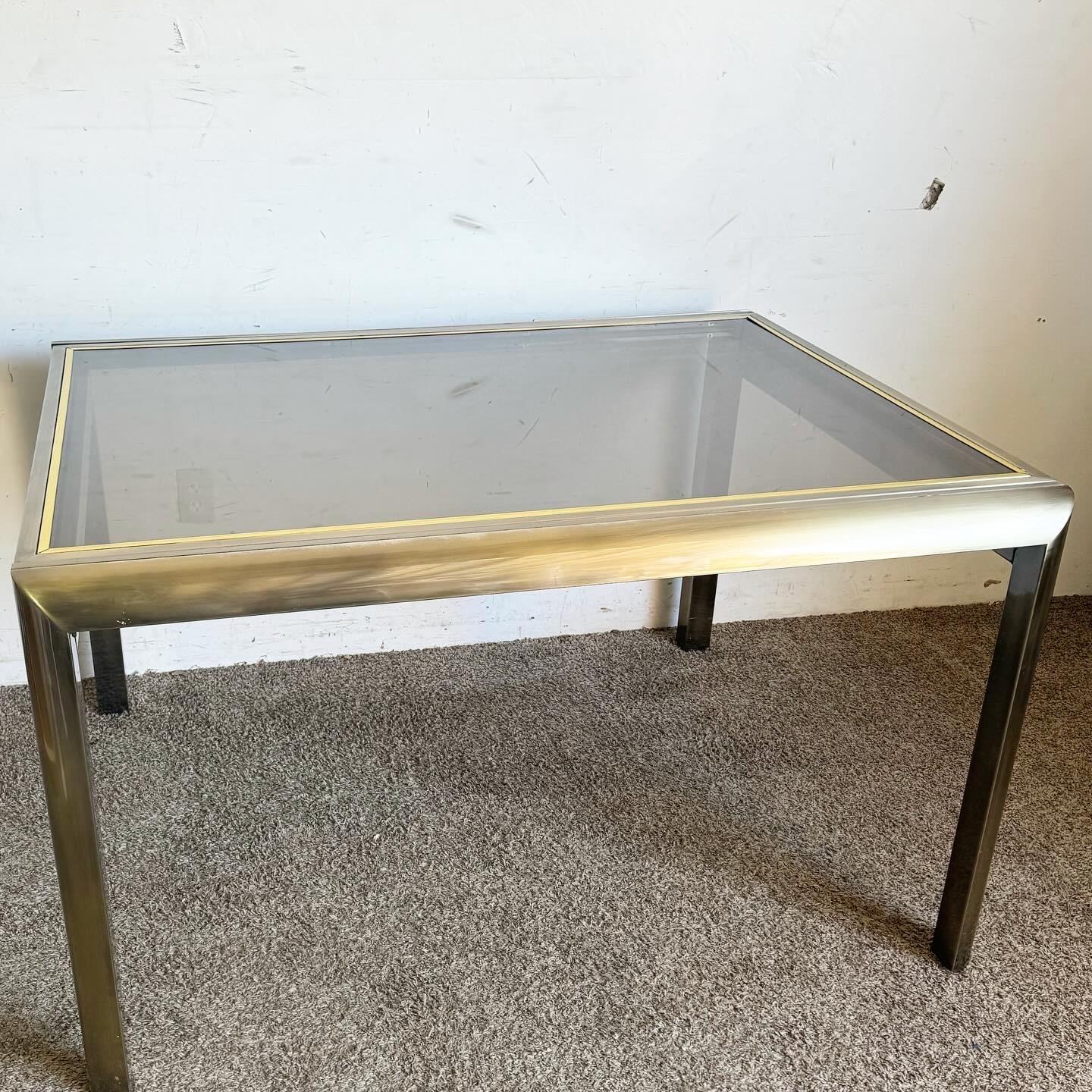 Delve into the postmodern elegance with this Brushed Brass Finish and Smoked Glass Extendable Dining Table by the Design Institute of America (DIA). Featuring a luxurious brushed brass frame and a sophisticated smoked glass top, this table combines
