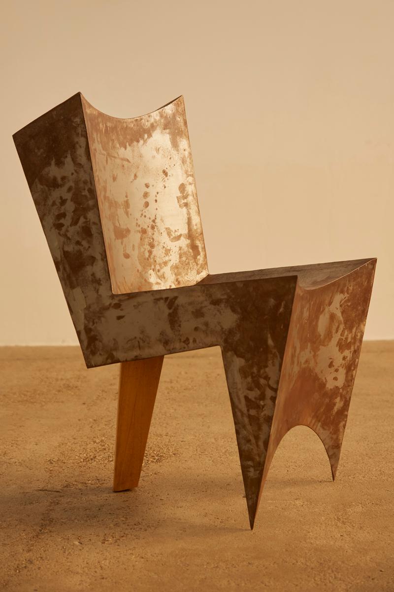 This unique postmodern chair, believed to be a one-off piece from the Netherlands, features a striking design with rusted steel surfaces and a single wooden rear leg. The clever construction creates the illusion that the chair is balanced solely on