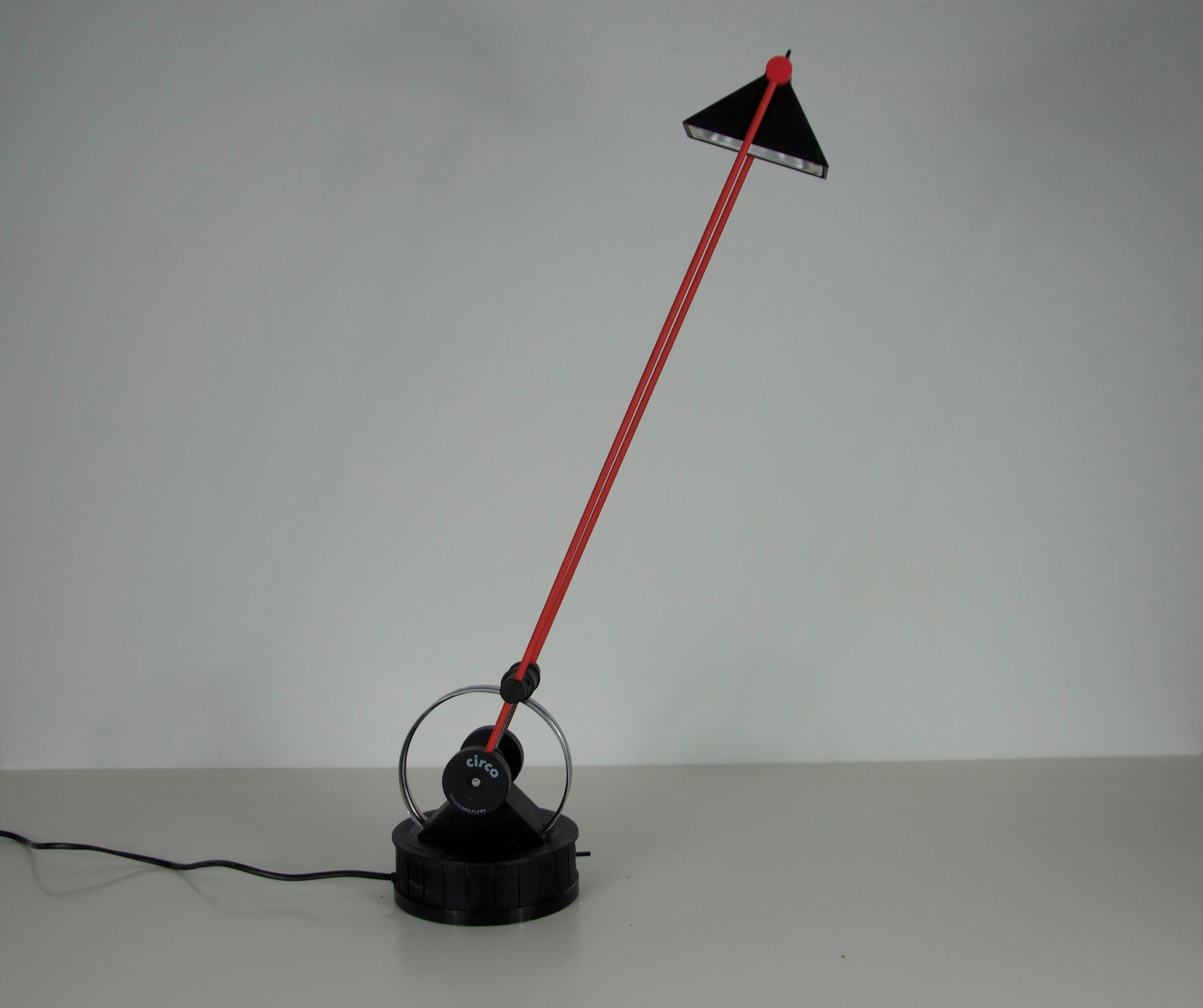 This striking red and black table lamp is a prime example of 1980s postmodern design. Exceptionally versatile, its adjustable arm moves freely around the circular base, while the base itself can rotate, and the triangular shade can be repositioned
