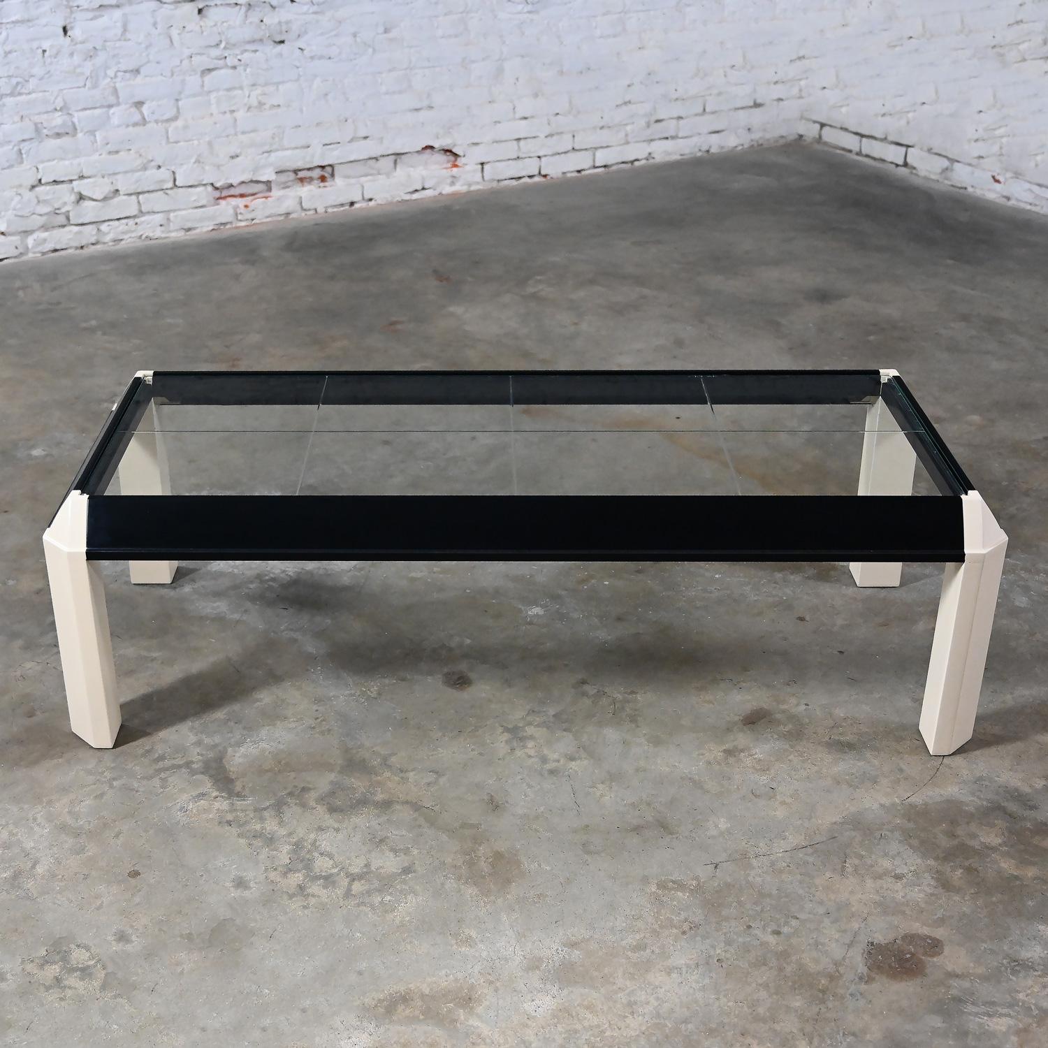 Handsome vintage Modern to Postmodern coffee table with trapezoid shaped legs, recessed glass top, and newly painted off white legs & corners and black painted rails. Beautiful condition, keeping in mind that this is vintage and not new so will have