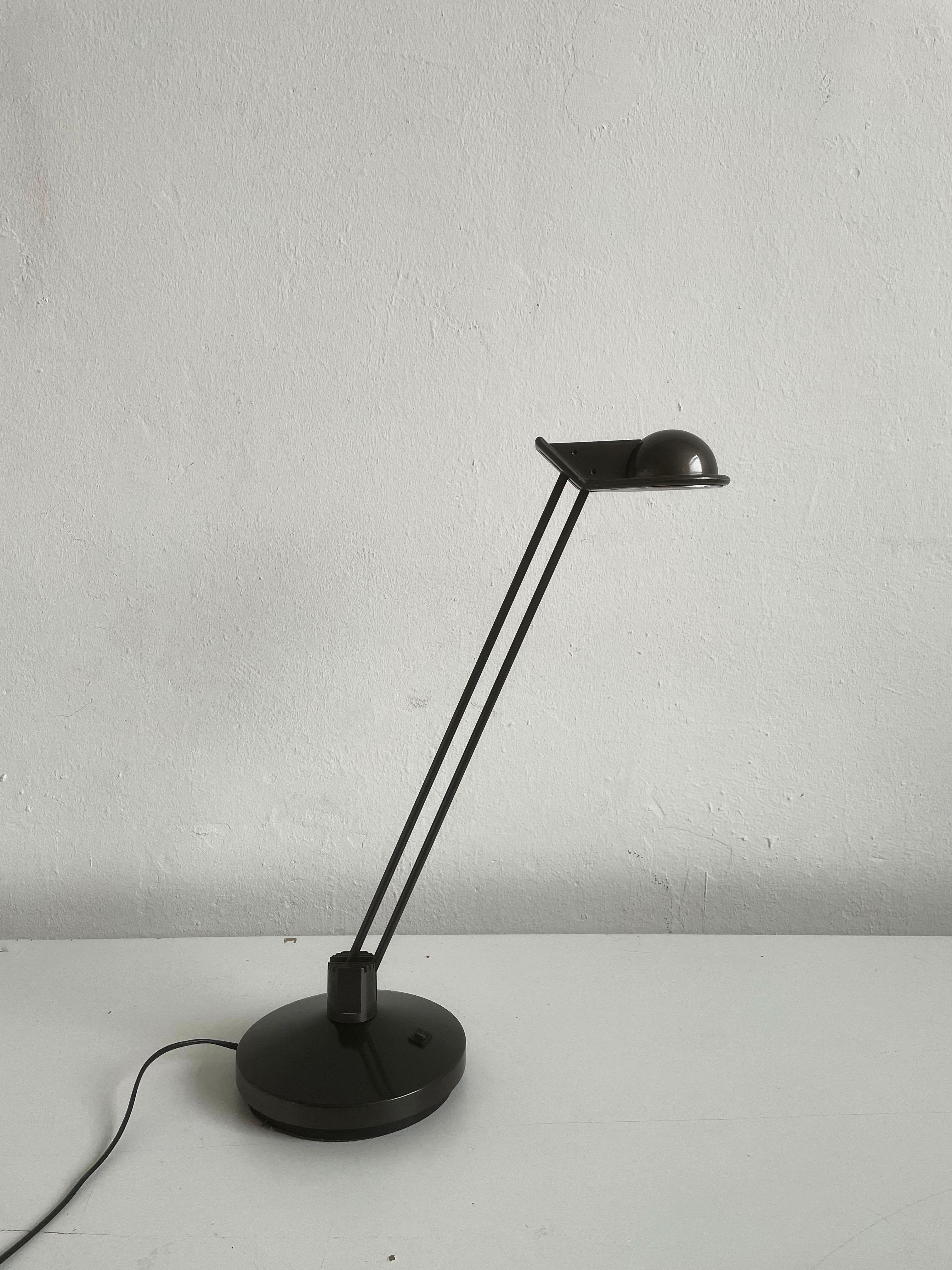 This table lamp was designed by Josep Lluscà for Metalarte in 1984. 

The dark grey halogen lamp has a rotating and adjustable arm and when inclining it, the lampshade remains horizontal in relation to the desk. 

This design was popular and a big