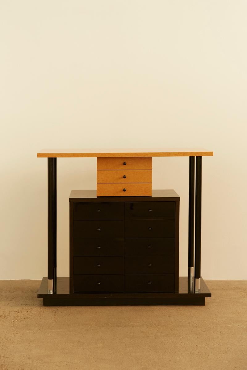 German postmodern cabinet, likely late 20th century, featuring black lacquered wood and burl wood accents. The design includes a rectangular tabletop on four black pillars, with burl wood drawers above a larger black lacquered storage unit. Also