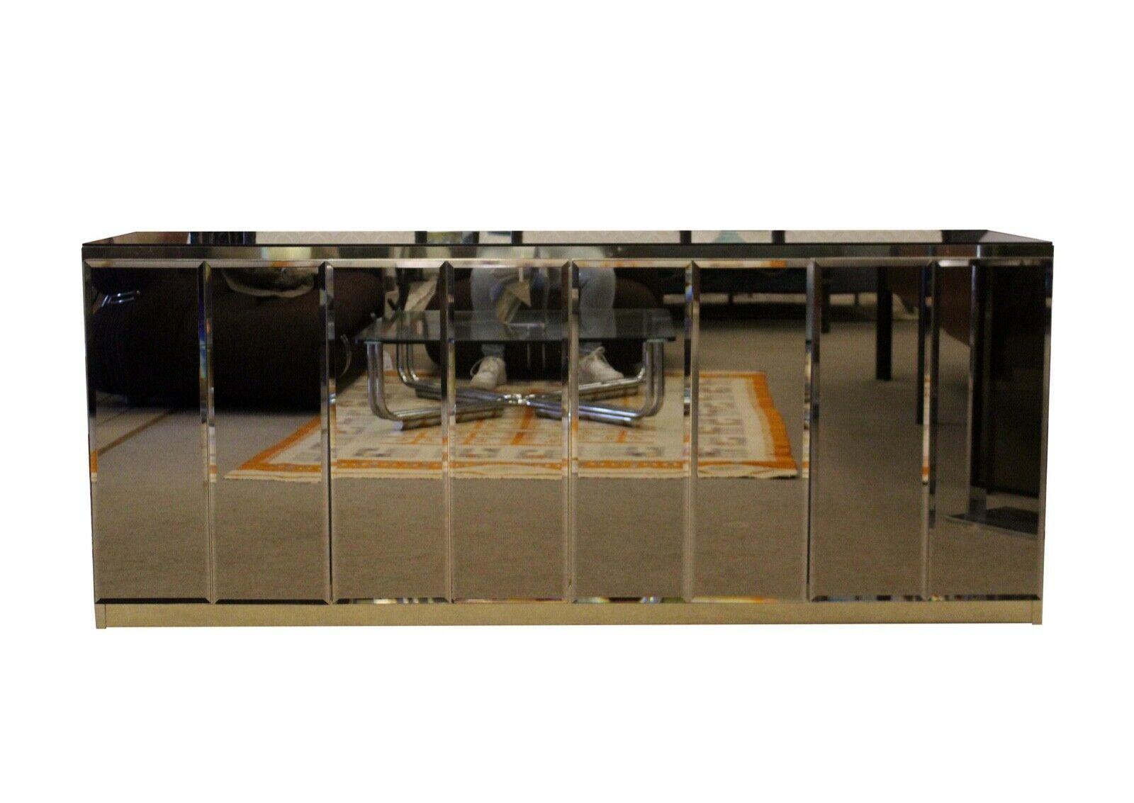 Ello is the iconic name in postmodern furniture. This credenza is fully finished with smoke colored mirrors on the front and sides and detailed with a gold toned veneer frame. The front fully opens providing shelving and ample