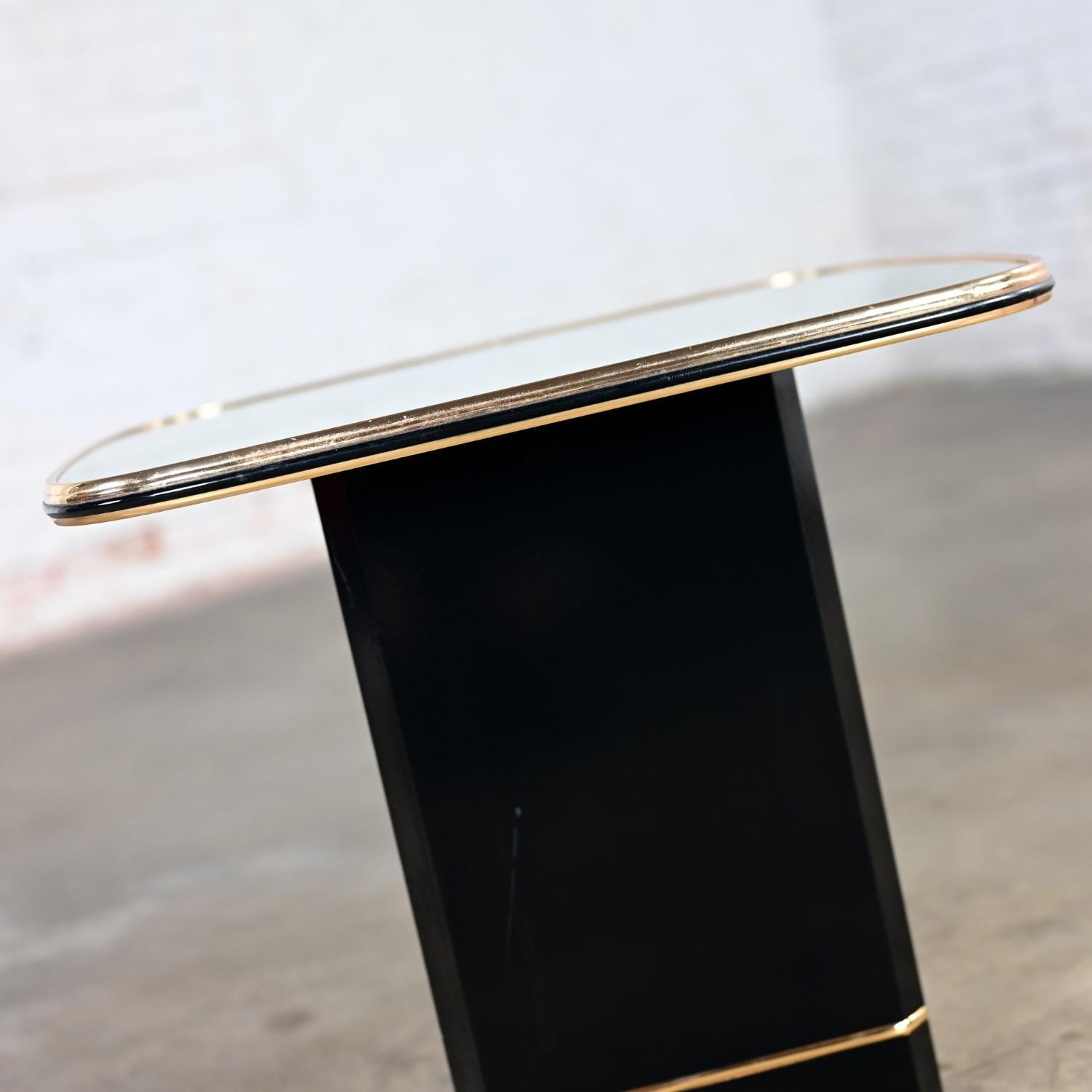Marvelous vintage Postmodern end or side table comprised of a black lacquered pedestal base with beveled edges & gold base trim and a rounded square shaped top with gold trim edges and mirror surface. Beautiful condition, keeping in mind that this
