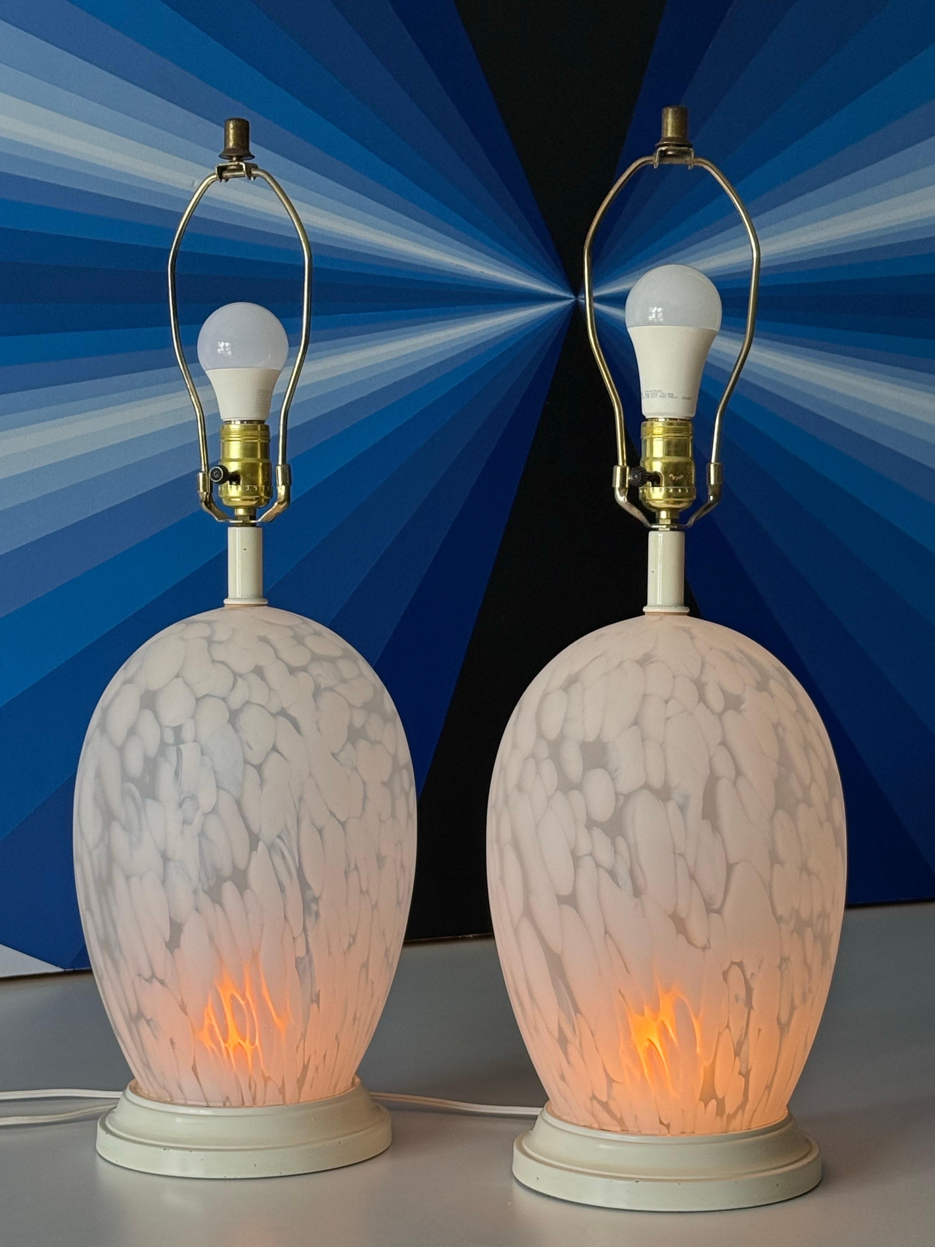 A pair of postmodern frosted glass lamps attributed to Murano, Italy. Quiet large oval shape made from glass with frosted glass detailing. Sitting atop round white bases.

This pair is on a three way switch giving the user options for brightness and