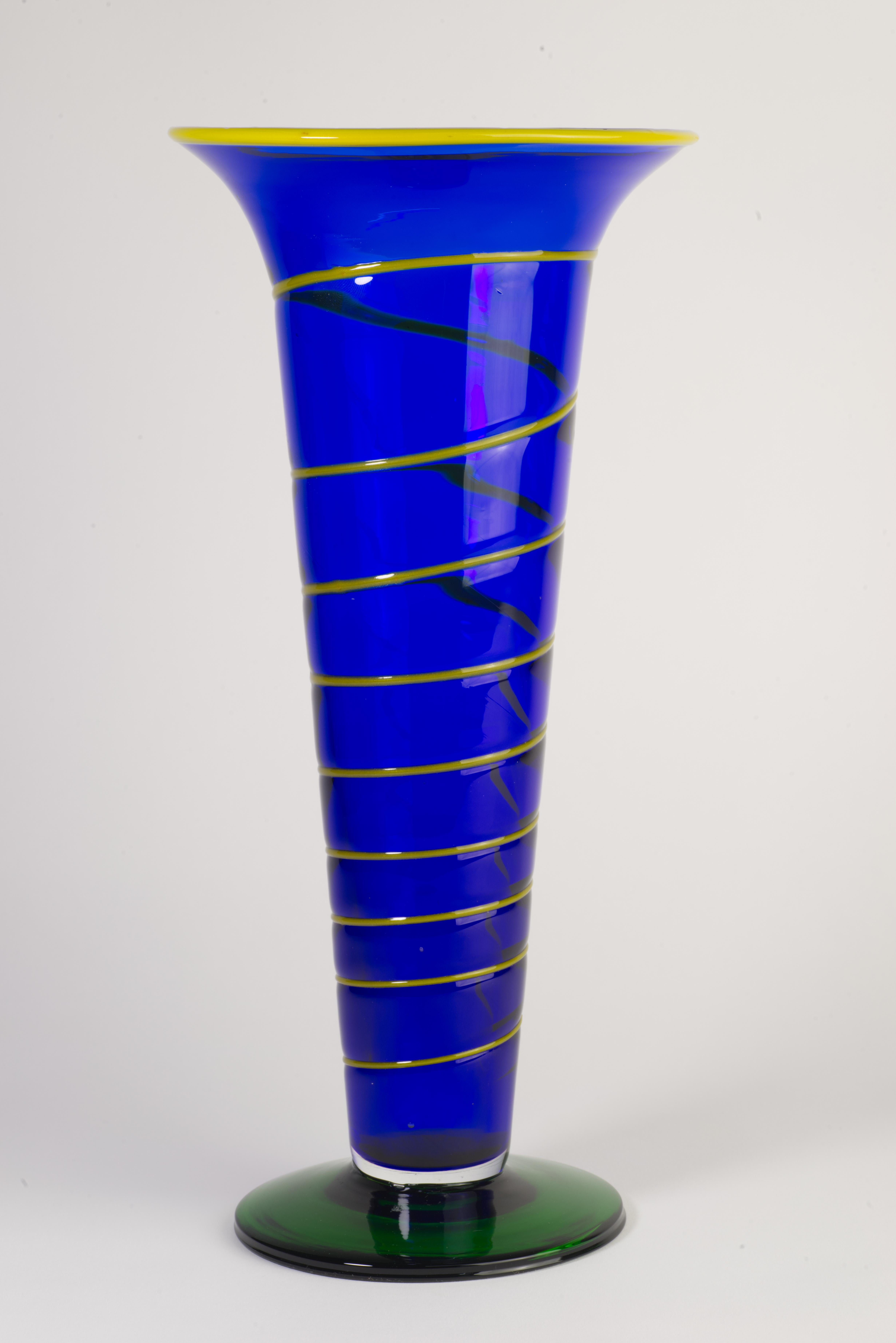 Sculptural, tall art glass vase was created in goblet shape with cobalt blue body encased in clear glass in sommerso technique; graphic yellow glass stripe was fused to the outer surface, circling around the piece and descending down to the dark