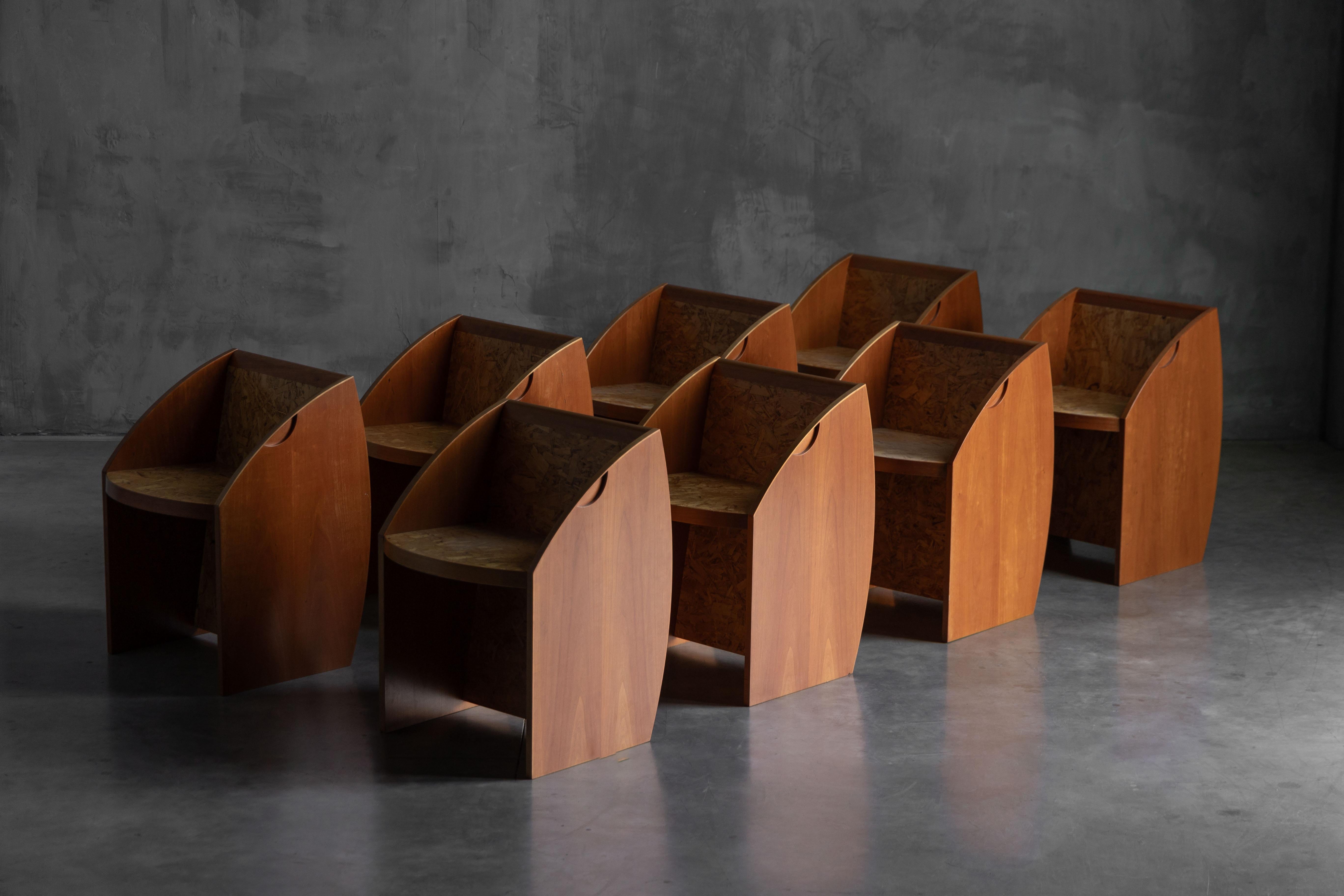 Rare postmodern chairs blending sculptural form with bold material contrasts. Each piece features a geometric silhouette crafted from rich wood, paired with pressed chipboard surfaces that emphasize texture and raw elegance. The arched sides and