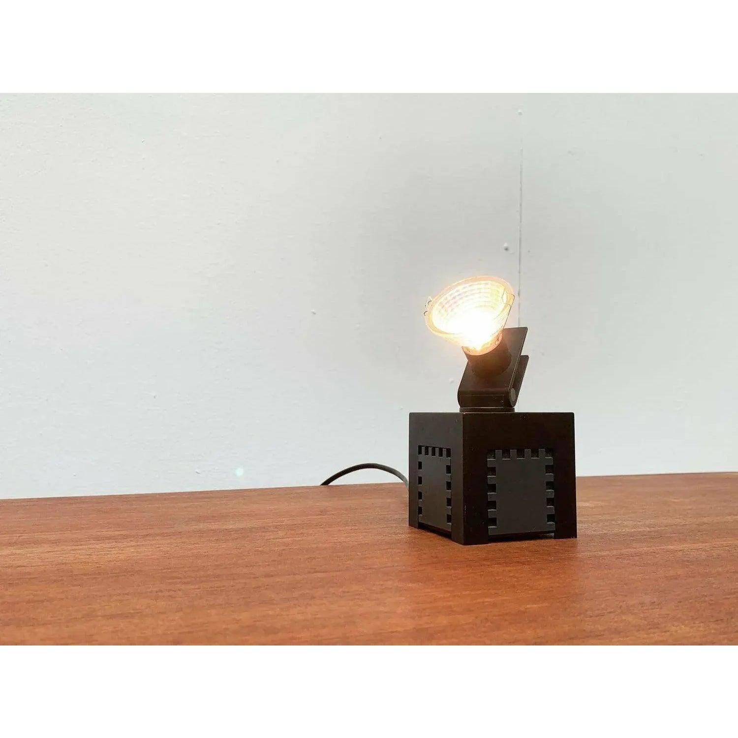 Postmodern table or wall lamp from Osram.

A functional design with postmodern details. The cubic base primarily consists of the cladding of the transformer. On the outside it is decorated all around with a graphic ornament. A narrow switch is