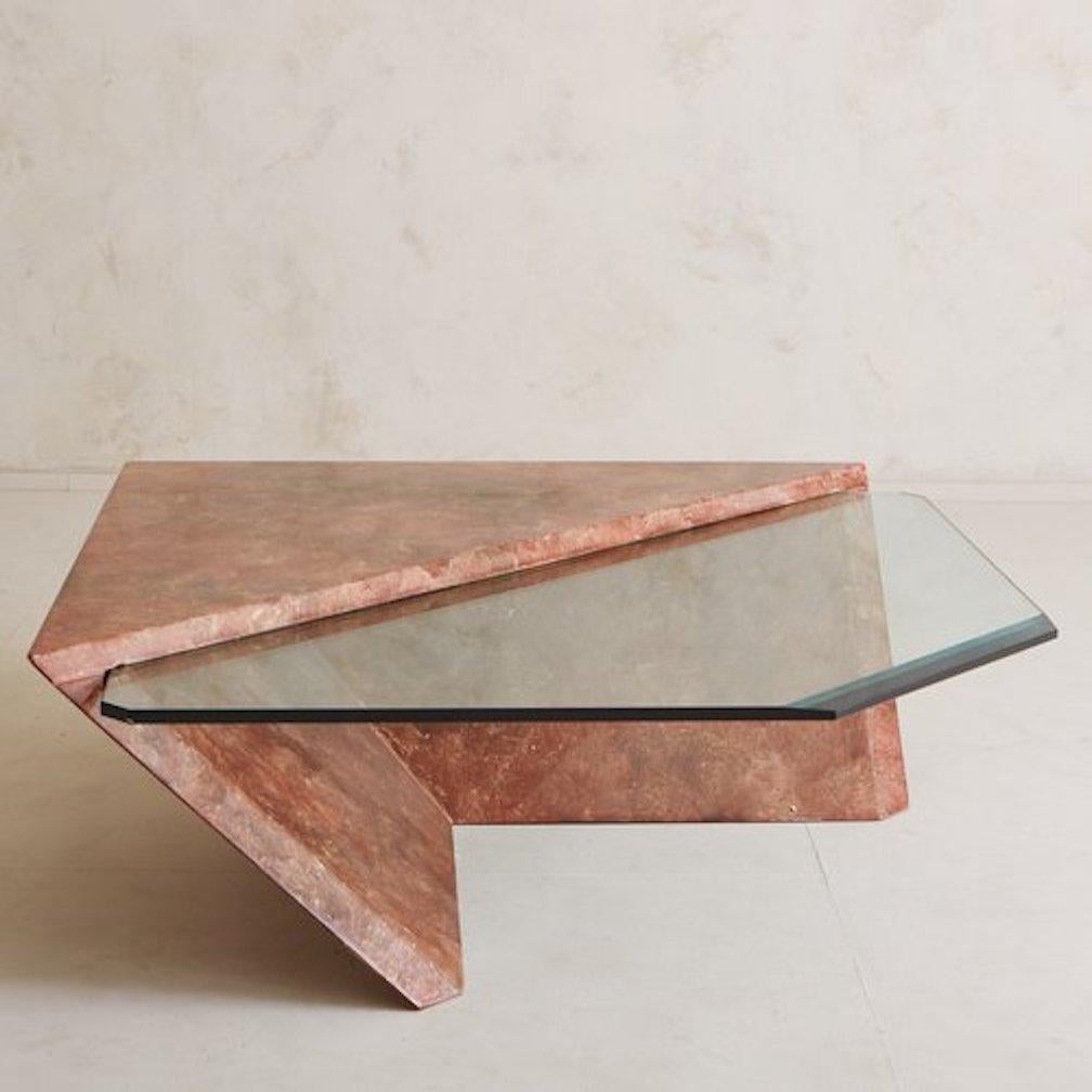 A Postmodern coffee table in the style of Roger Rougier featuring a dramatically angled faux marble laminate base in a beautiful coral hue. This table has a glass top that is counterbalanced by the base. USA, 1980s.