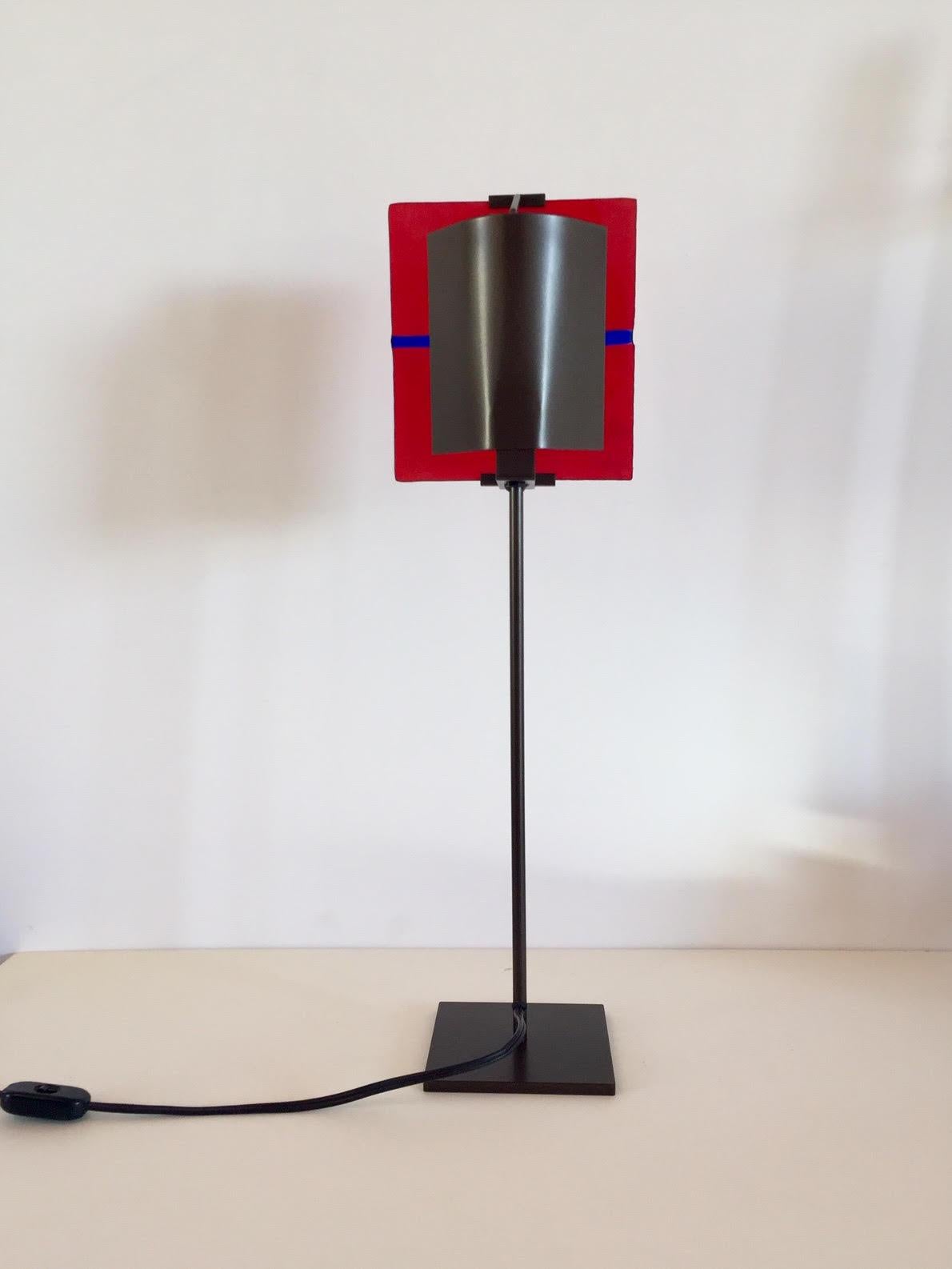 Original and unique table lamp, Postmodern in style (circa 1990s). Original piece that is minimal and modern. Bold in form and bright in color. This piece consists of an iron base that holds a handcrafted glass tile in red with a blue line across