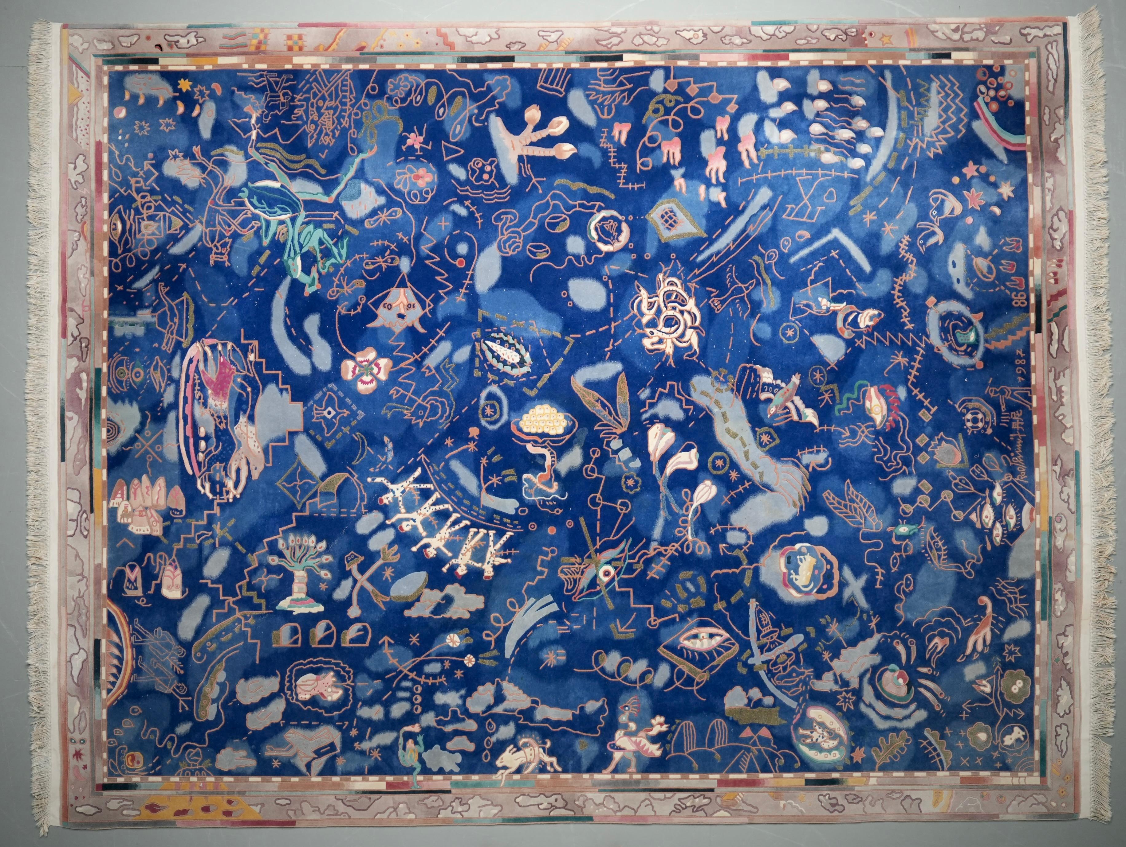 Large hand-knotted rug in wool, signed and dated 1986, 1987. The design is full of energy, with a deep blue ground and many surreal details. You see snakes, birds, trees in bloom, winged figures, stars and abstract shapes, almost like a dreamscape