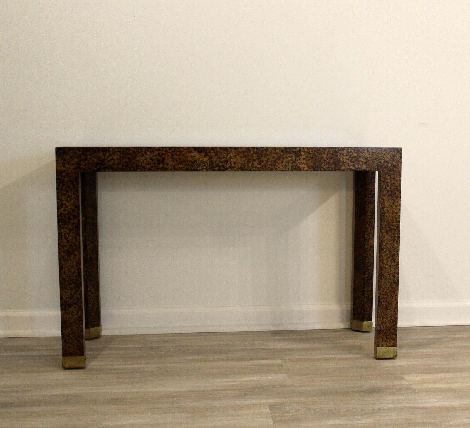 Faux tortoise shell framing creates a sophisticated, dimensional look in this Parsons style console table which is detailed with a smoked glass surface and finished with brass ferrules on each foot. This postmodern console table will work well with