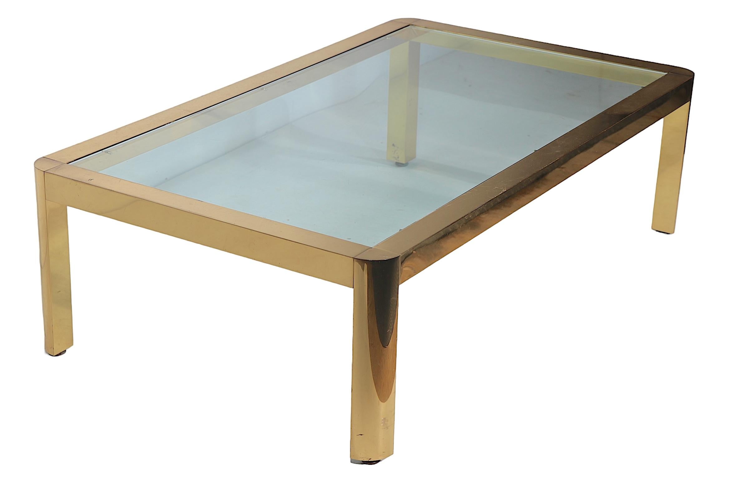 Voguish, chic, and sophisticated brass and glass coffee table having a bright brass frame of squared stock, with a thick tempered glass insert top. The table is in very fine, original, clean and ready to use condition, showing only light cosmetic