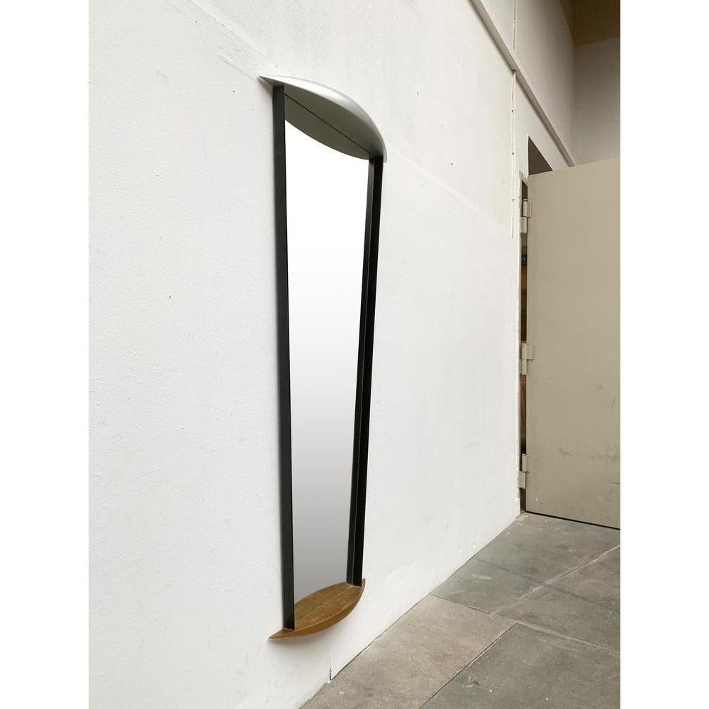 A mirror of imposing size and heavy quality. A metal plate serves as a support. The mirror surface is bordered and widens upwards. On the sides there are black moldings. Above and below boat-shaped elements as ornament. The lower element is