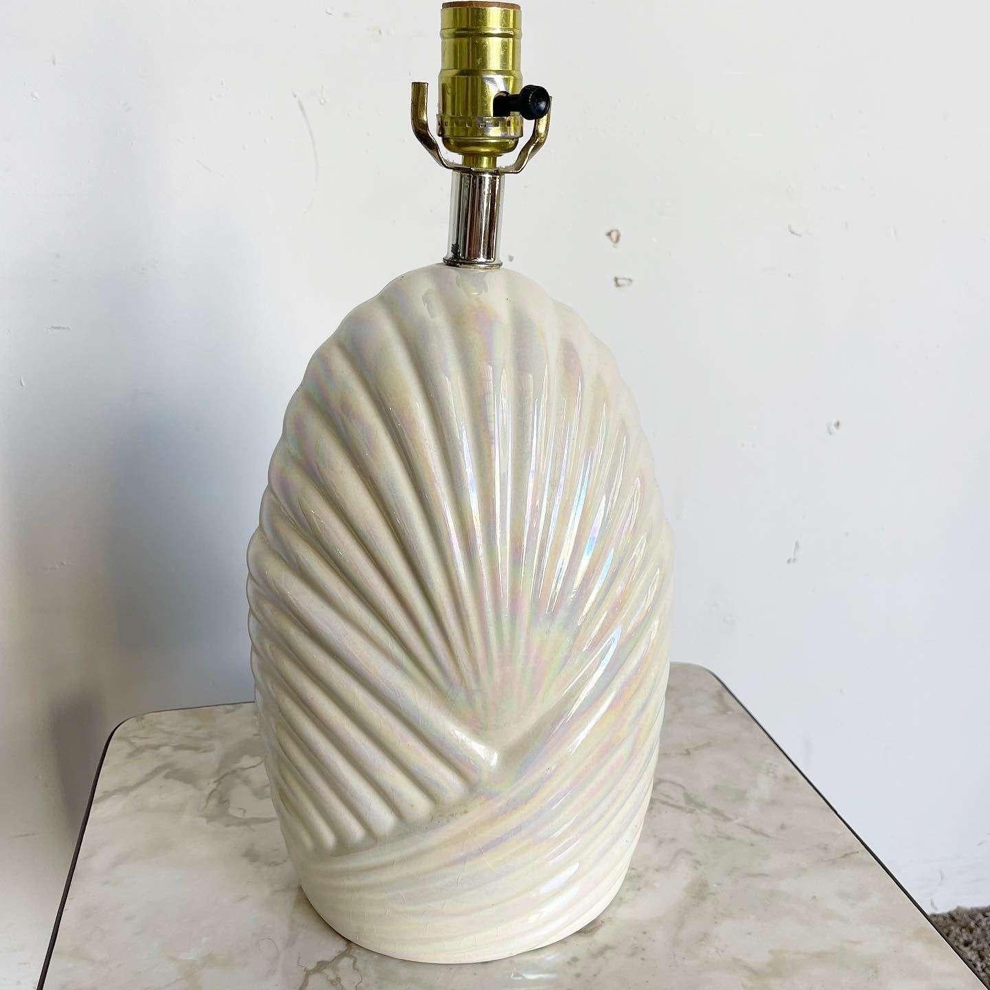 Illuminate your space with the captivating charm of this amazing vintage postmodern ceramic table lamp. The lamp showcases a scalloped body with an off-white iridescent finish, exuding a unique and mesmerizing aesthetic. With its blend of vintage