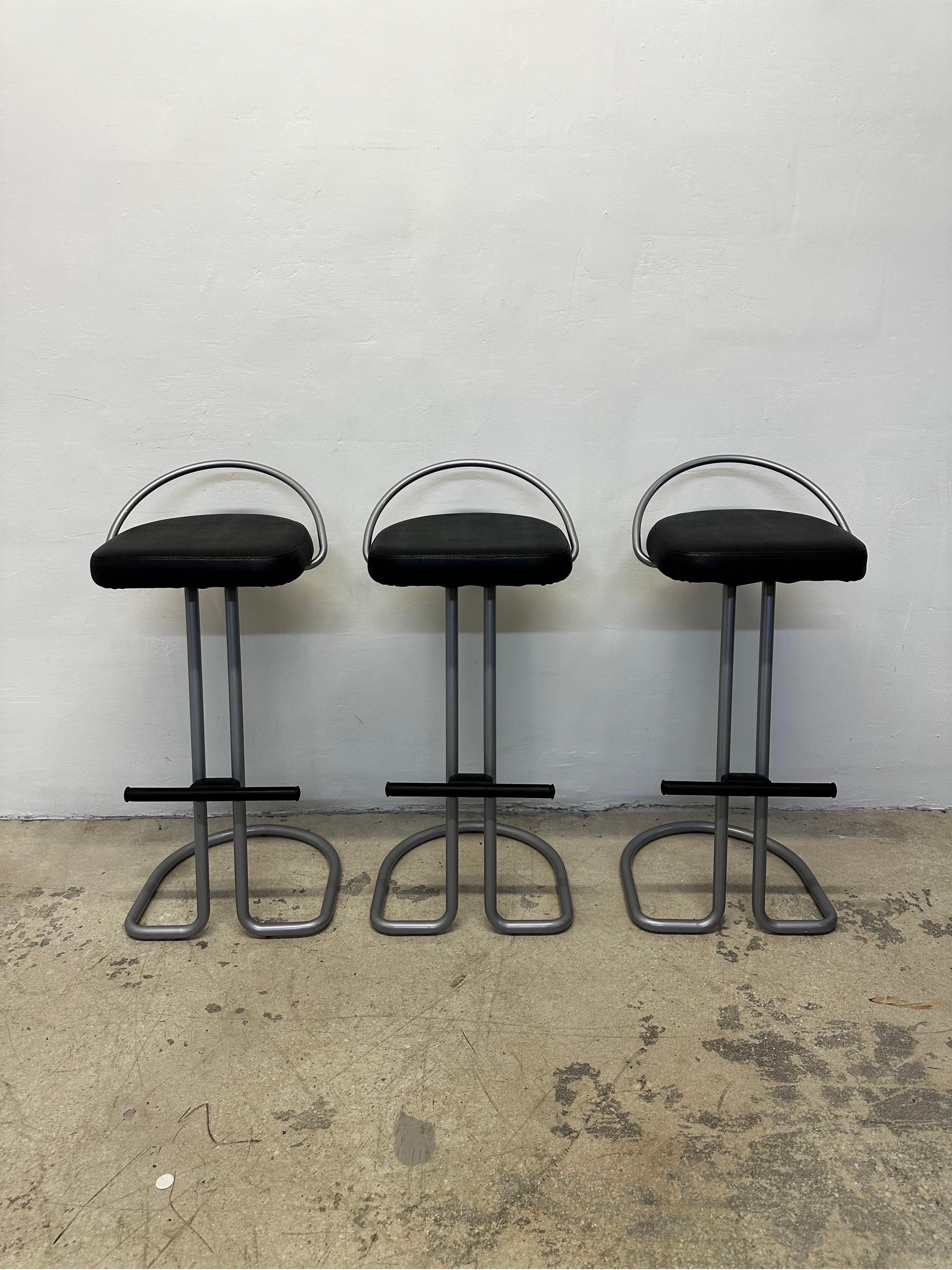 Set of three postmodern Italian barstools with black Naugahyde seats and silver lacquered frames with footrests.
